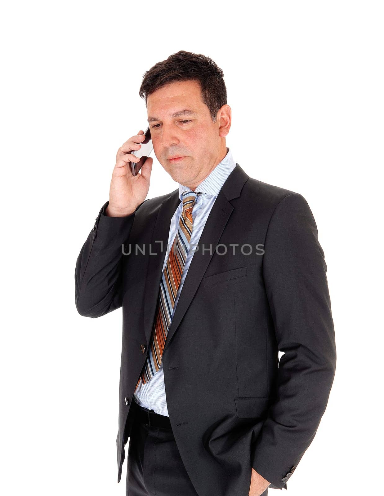 A handsome businessman standing in a dark suit with one hand in his.pocket, talking in his cell phone, isolated for white background.