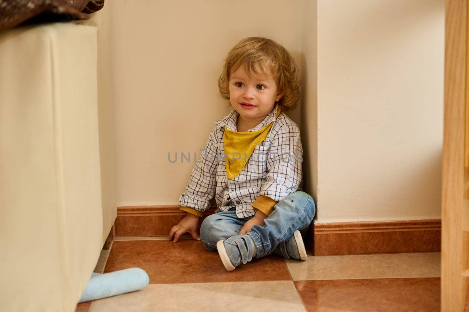 Young child indoors, seated in a corner, joyfully interacting. The playful environment and casual attire evoke innocence and comfort.