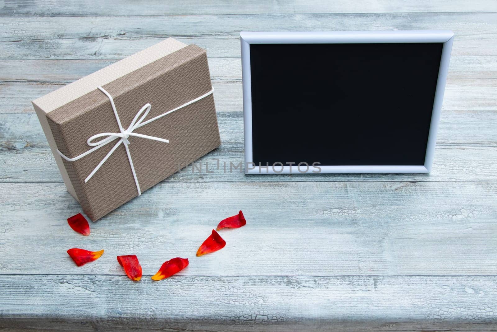 Gift box with an empty picture frame with place for your text and tulips leaves on rustic bright wooden table. Card concept.