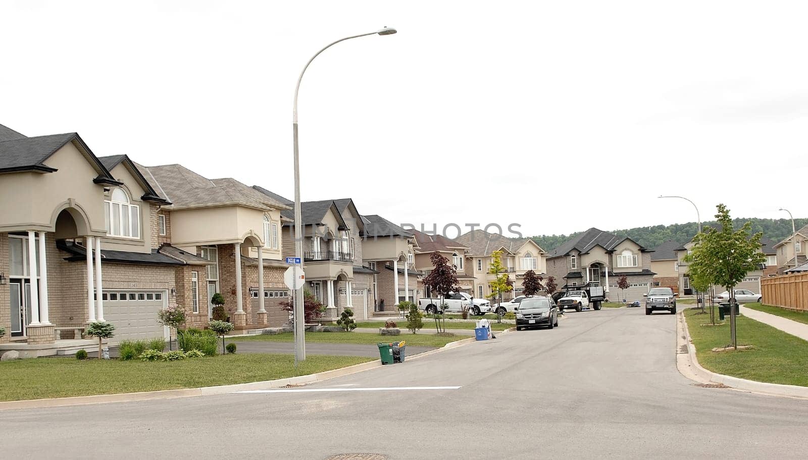 A suburban street with new big houses in the summer time whit cars.in the drive way.