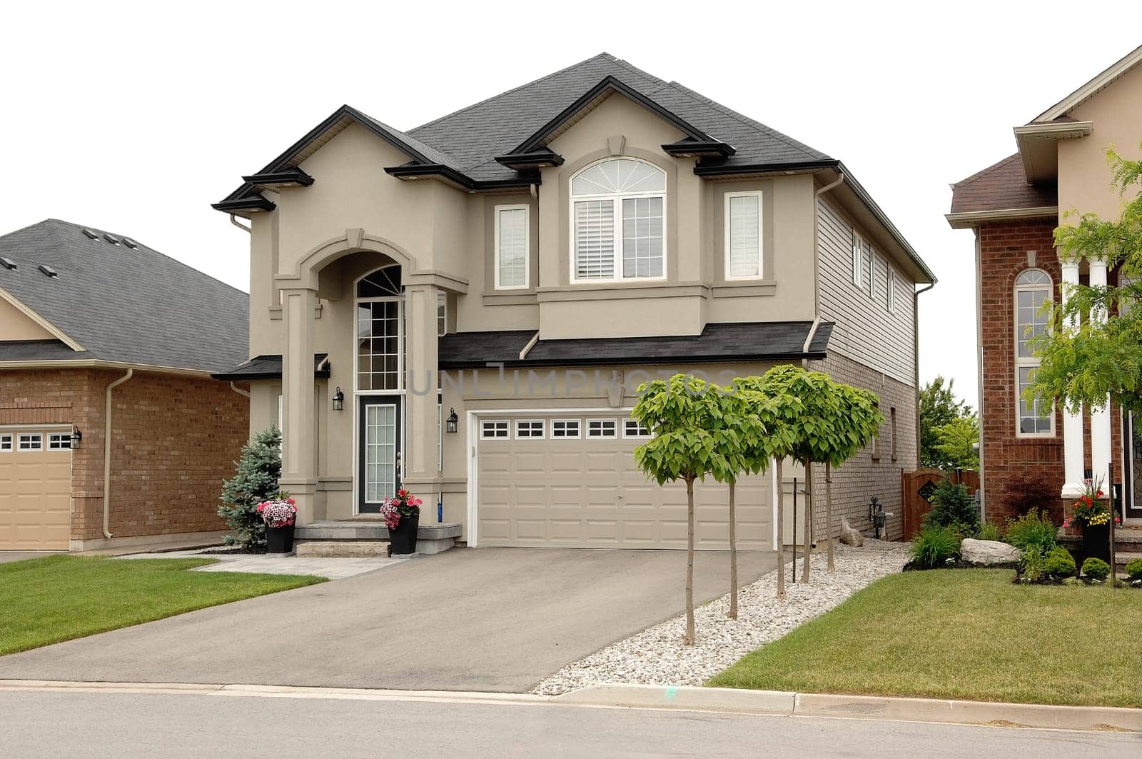 A new big two story house in a subdivision in Hamilton, Canada, .with a two car garage and small trees.