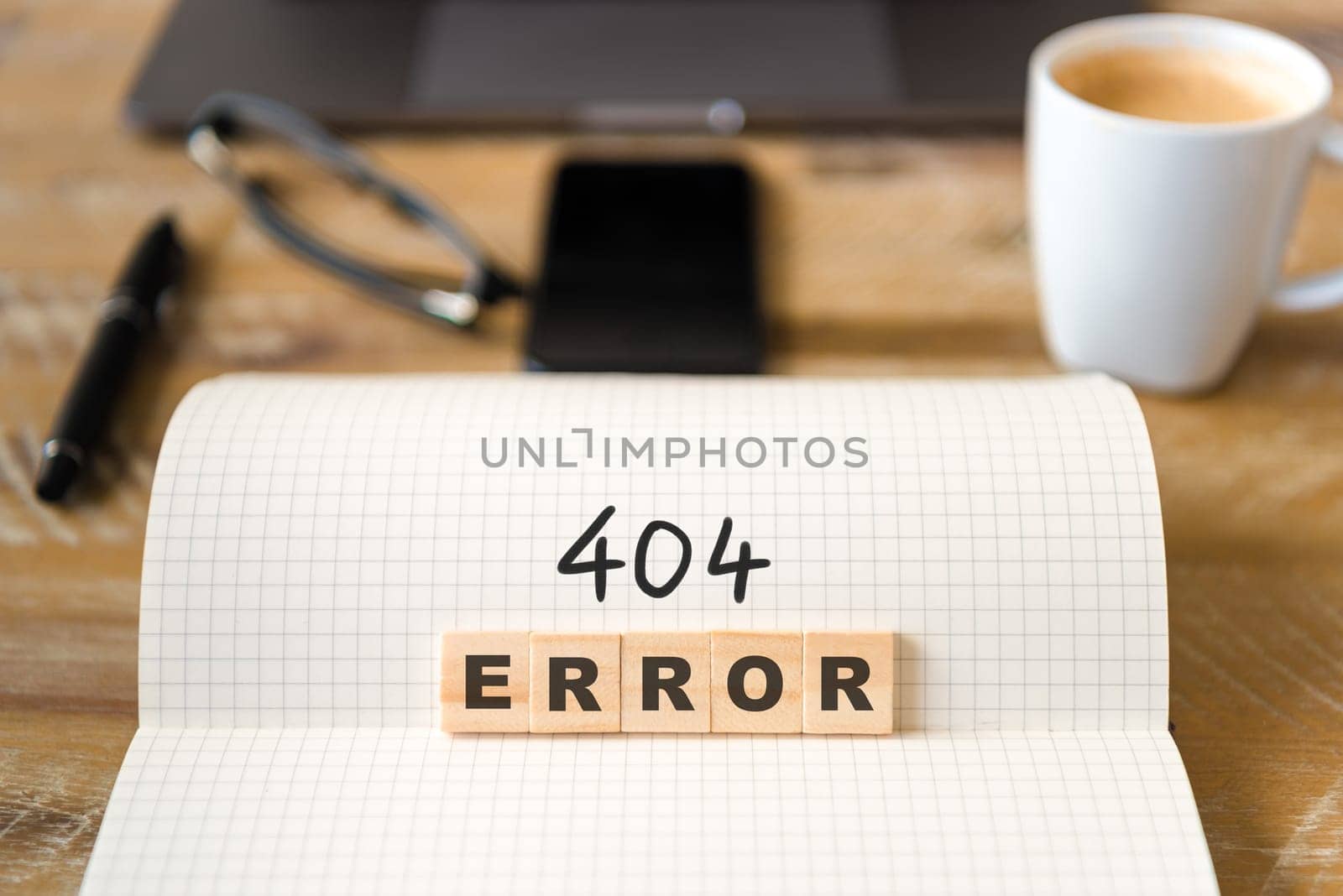 Closeup on notebook over vintage desk surface, front focus on wooden blocks with letters making 404 Error text. Business concept image with office tools and coffee cup in background