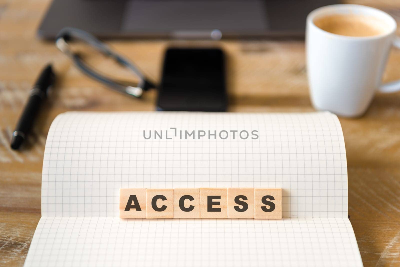 Closeup on notebook over vintage desk surface, front focus on wooden blocks with letters making Access text. Business concept image with office tools and coffee cup in background