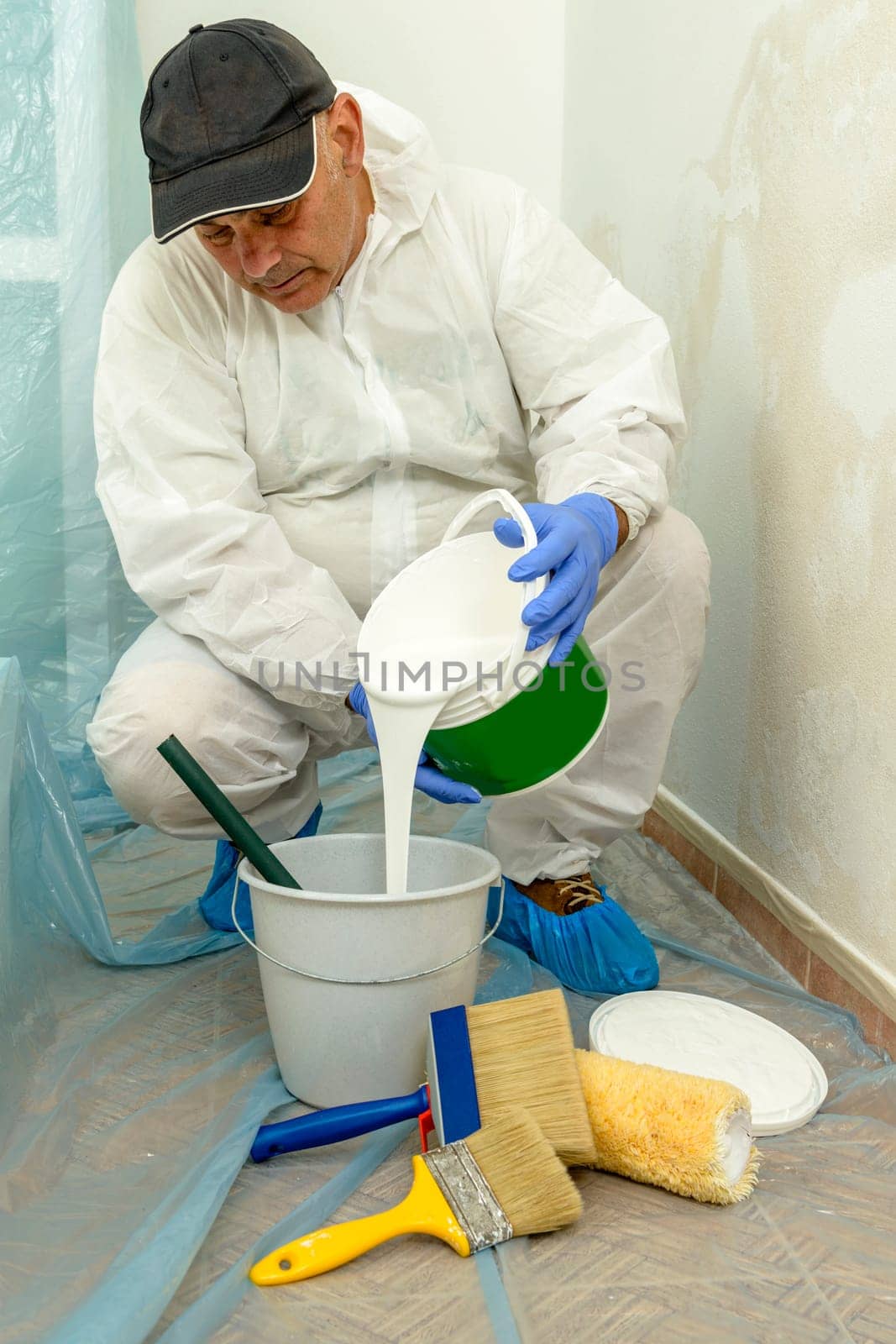 Painter paints the wall with the tint of white. Wall with serious moisture problems. Detail of the brush. white dye is prepared for the painter's job.