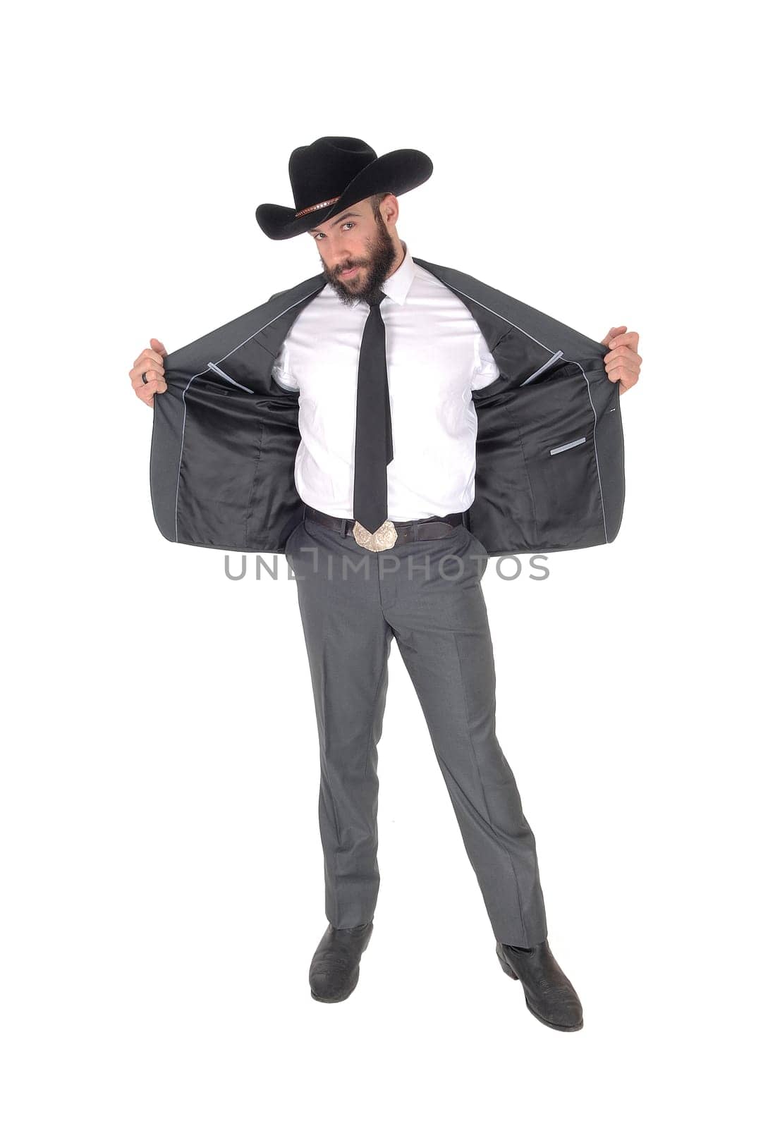 A handsome man standing in a gray suit and cowboy hat opens his.jacket, with beard and mustache, isolated for white background.