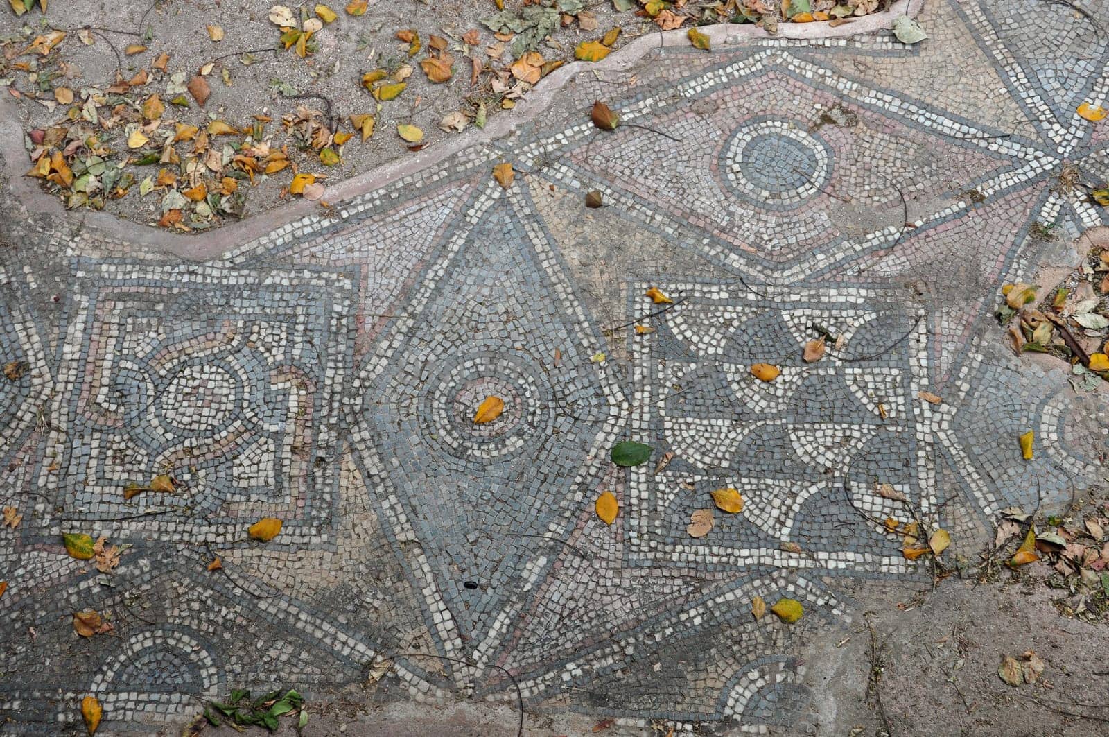 Ancient floor roman mosaic geometric shapes motif abstract pattern and fallen leaves. Athens, Greece.
