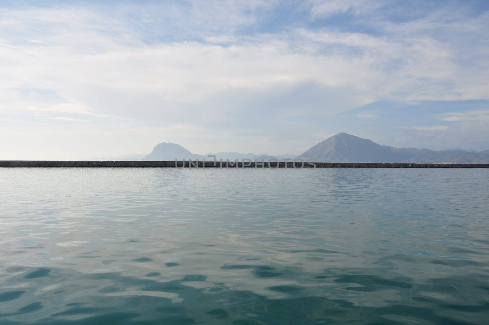Distant hills sea and cloudy sky horizon landscape. Seawall pier on port of Patras, Greece.
