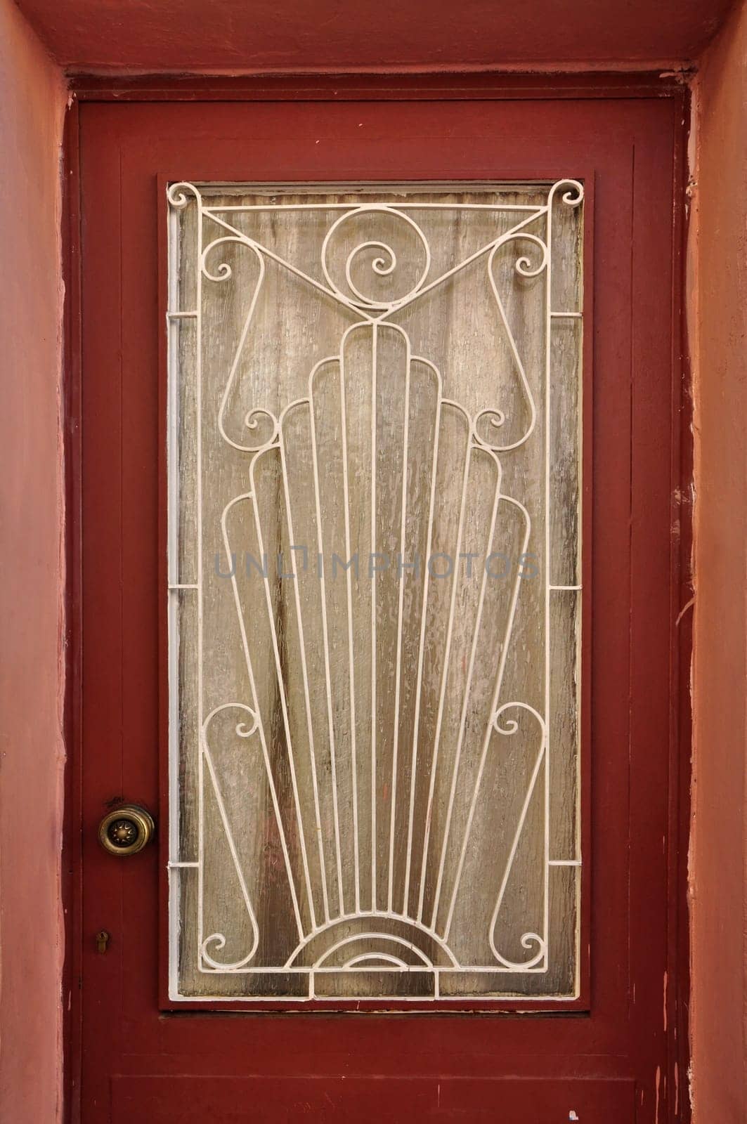 Old wooden door glass lite screen decorated with iron pattern of abstract sun rays and spiral symbols.
