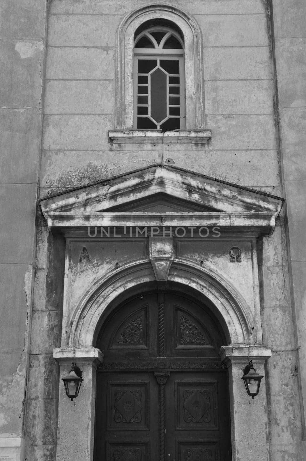 Byzantine church exterior with alpha and omega engraved inscription. Arched wooden gate and weathered wall black and white.