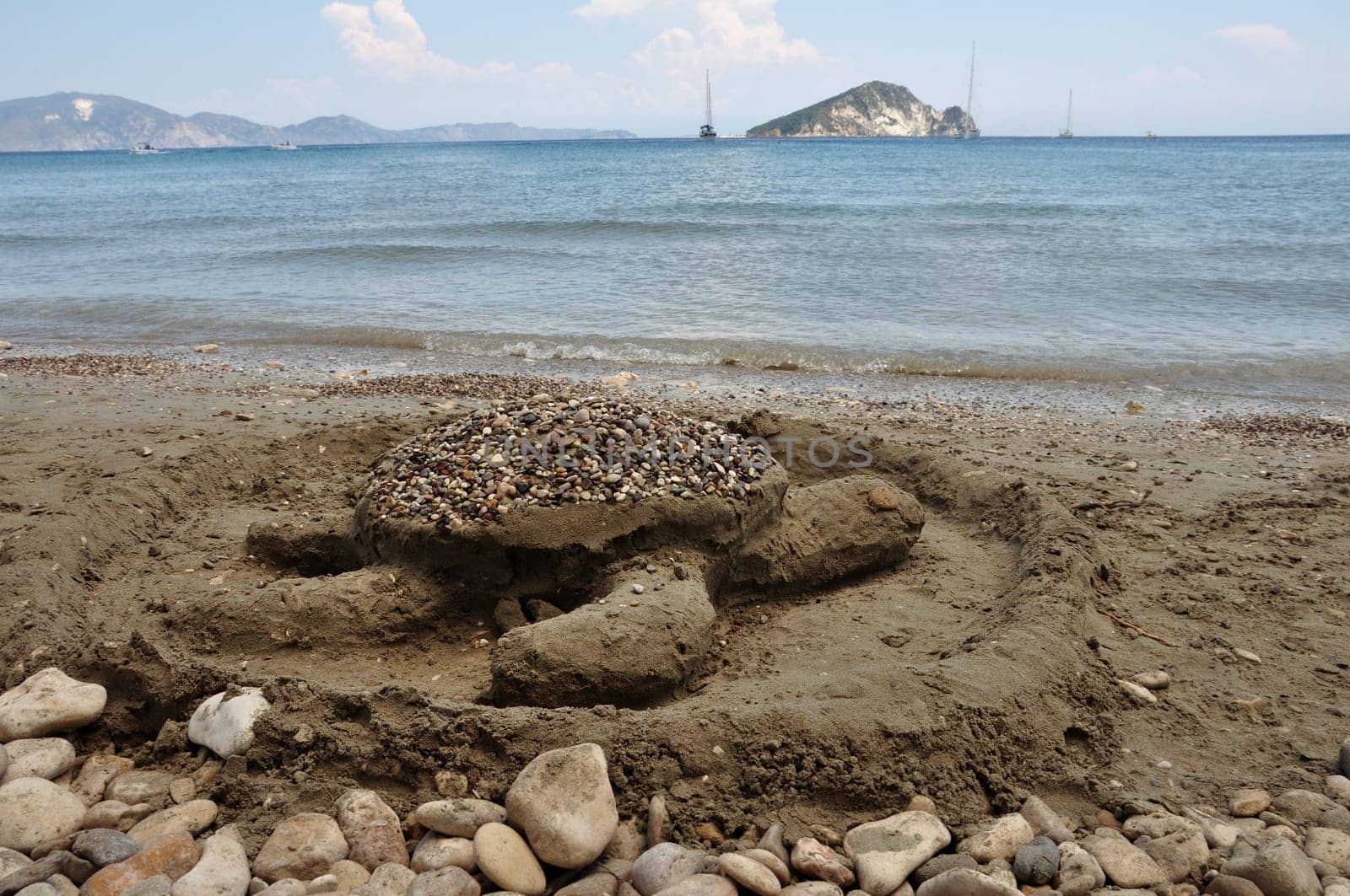 Loggerhead sand sculpture on Keri beach and distant view of Marathonisi islet shaped like a gigantic sea turtle and favorite nesting ground of the caretta caretta. Zakynthos, Greece.