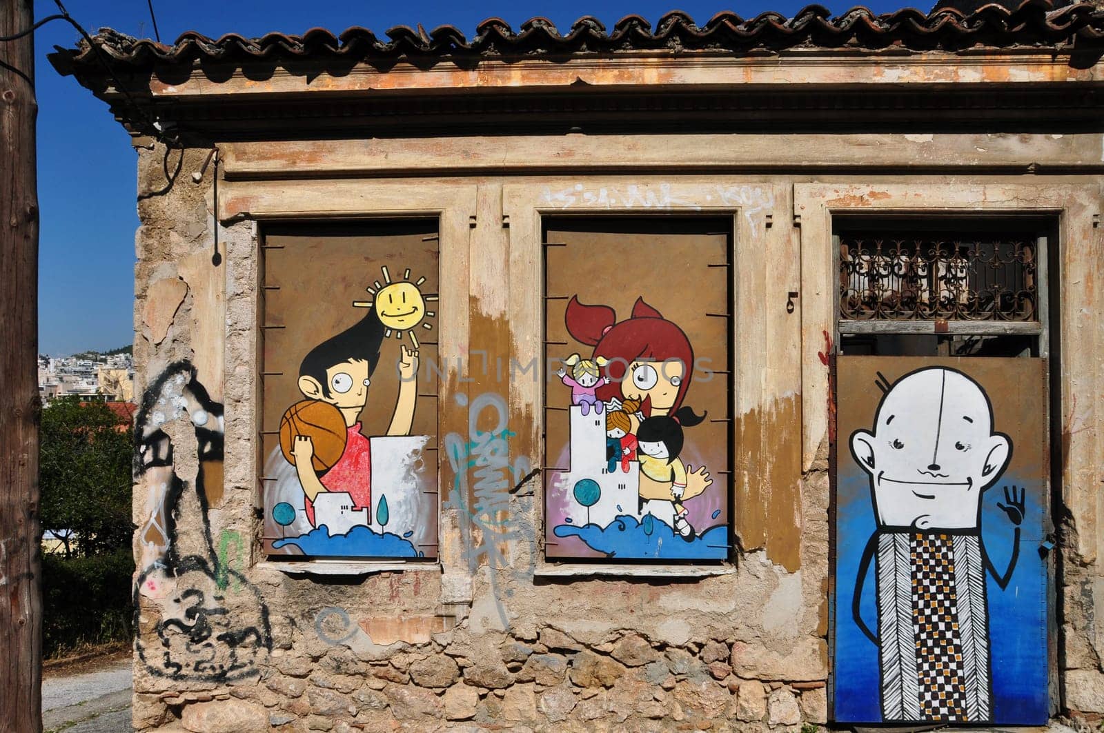 ATHENS, GREECE - APRIL 15, 2014: Colorful graffiti happy cartoon characters on the boarded up windows and door of an abandoned house in Plaka.