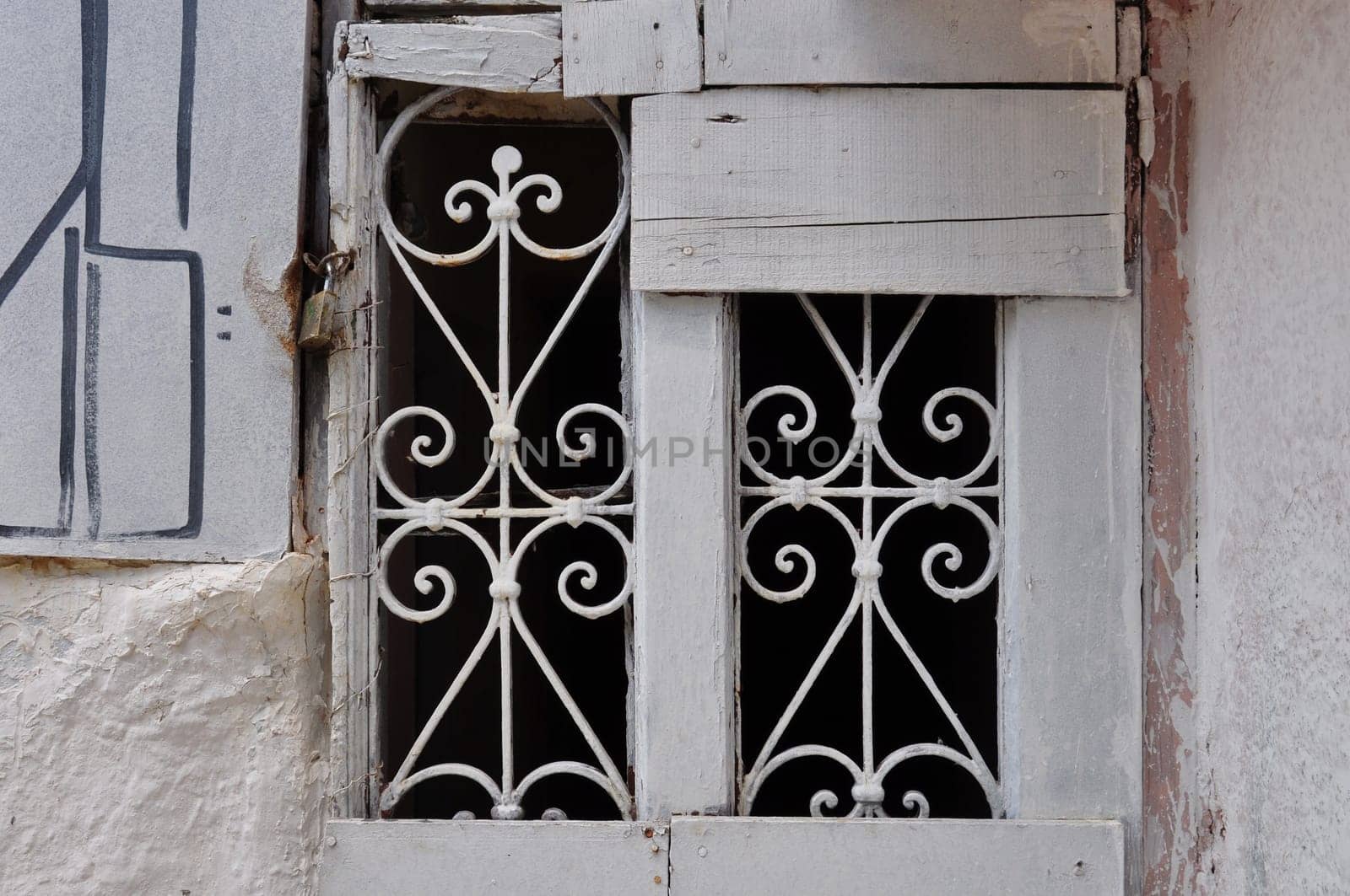 Old window with decorative metal motif. Abandoned boarded up house.