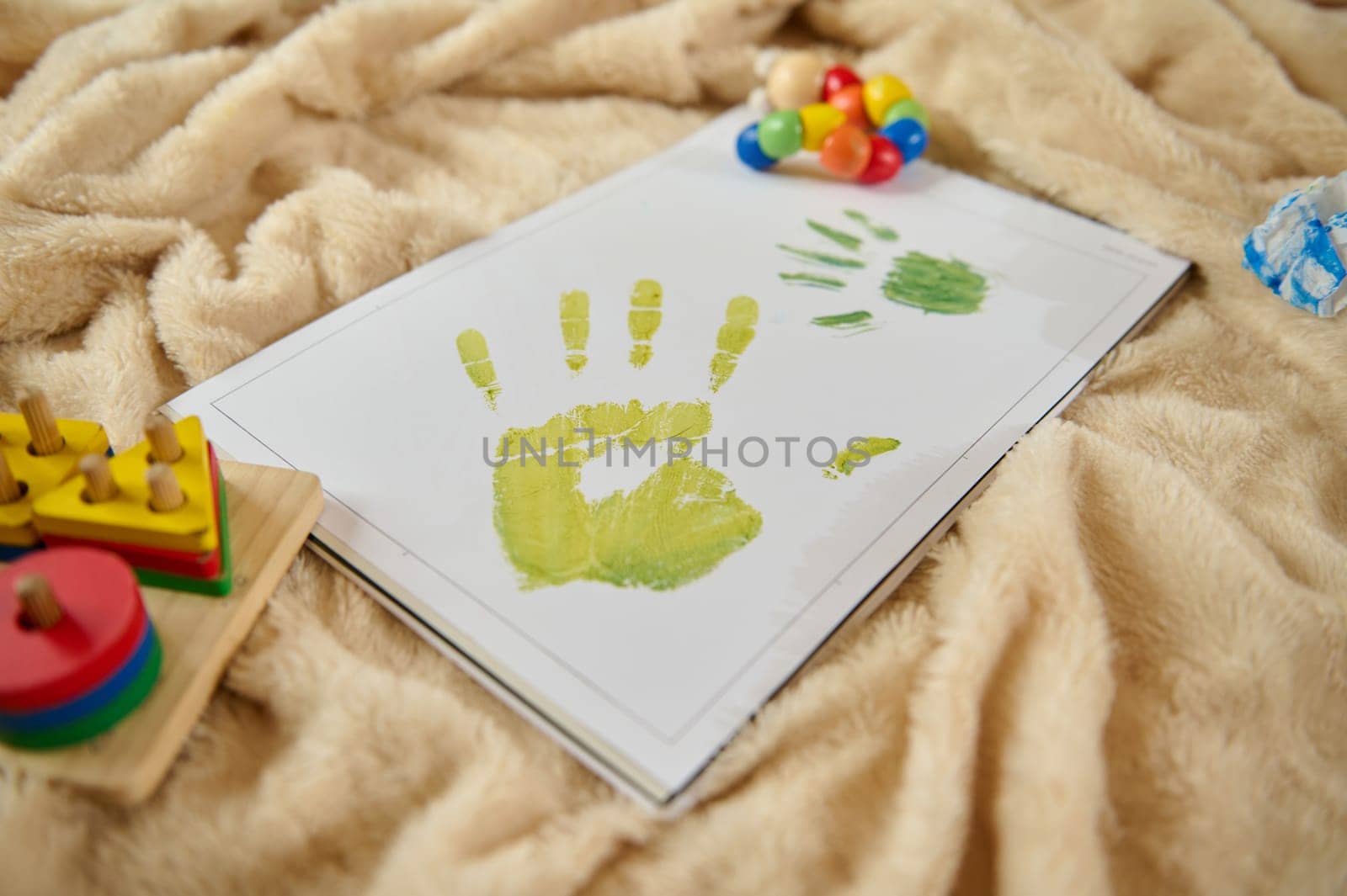 Colorful child handprint artwork adorning a sheet on a cozy blanket surrounded by toys representing creativity, play, and joyful moments.