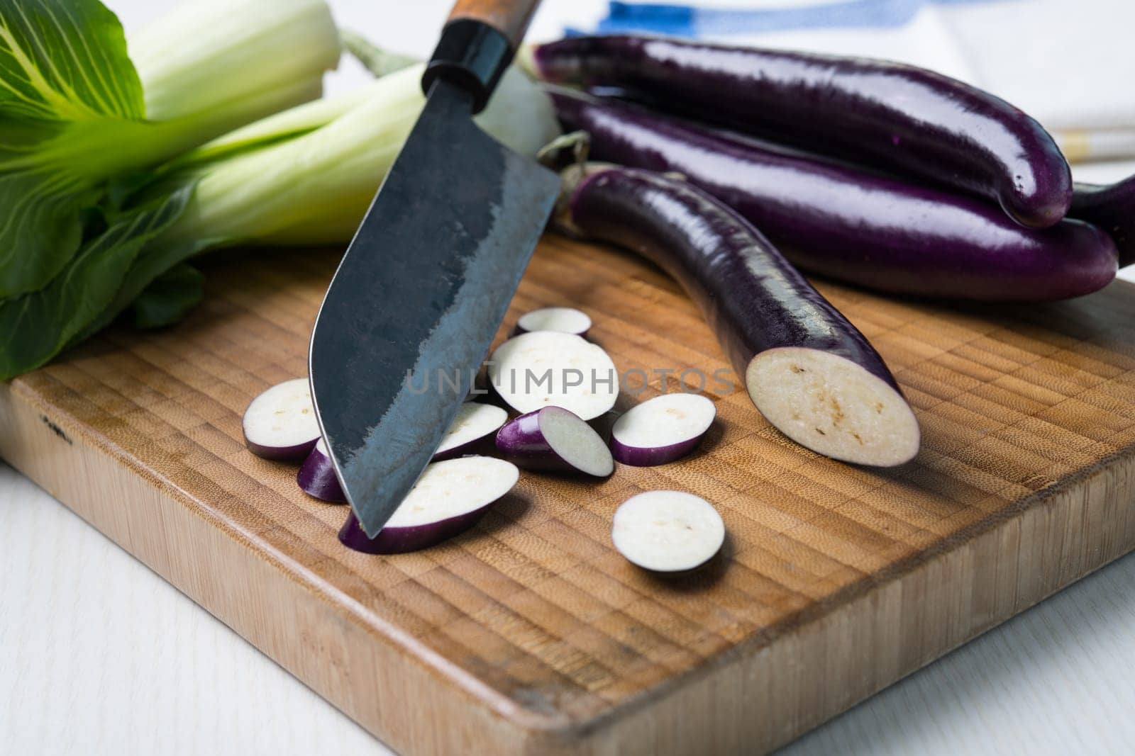 japanese eggplant on wooden board with cooking knife and pak choi salad