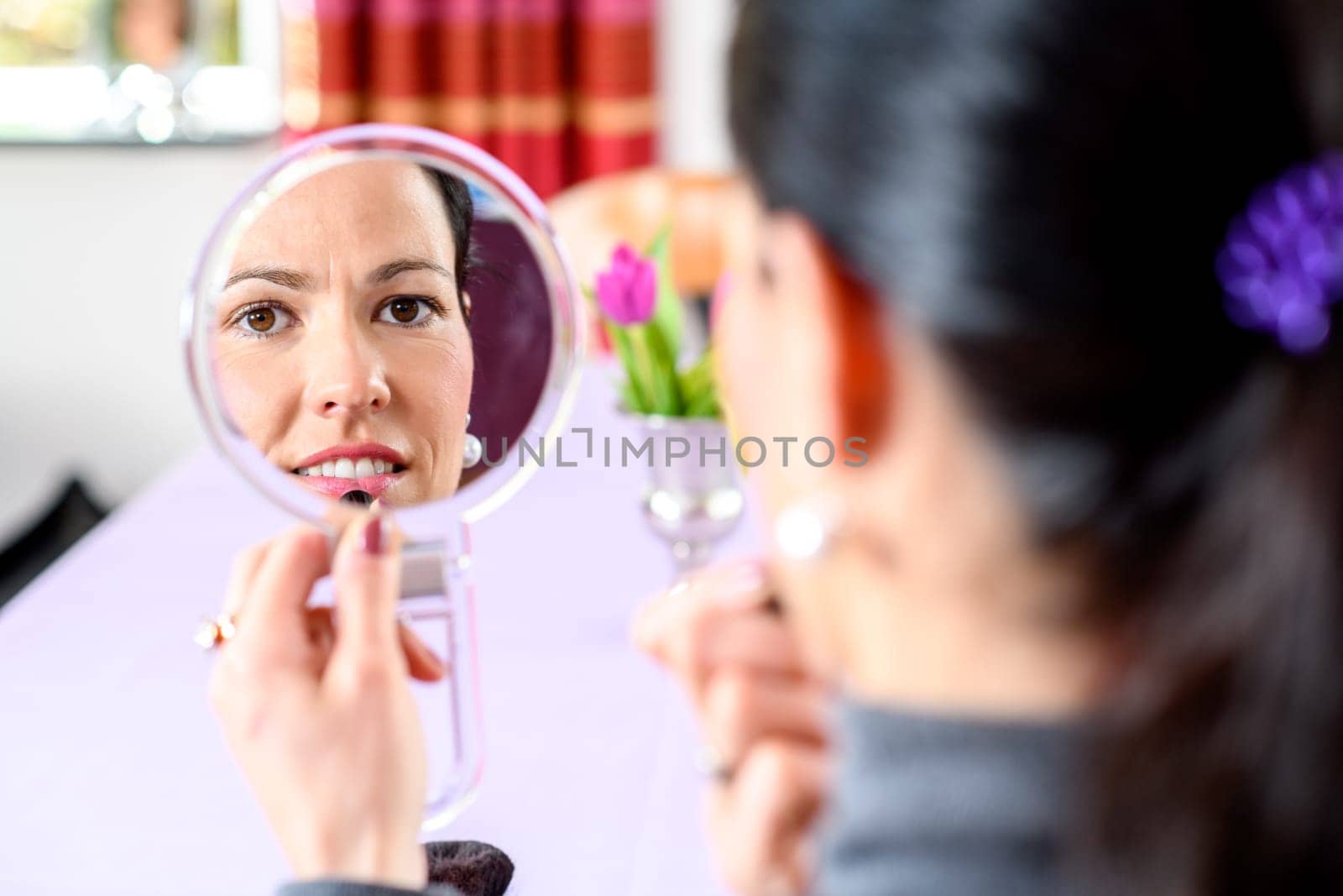 young dark haired woman looking in mirror and applying make up