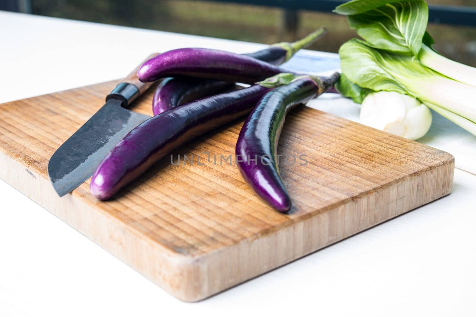 japanese eggplant on wooden board with cooking knife and pak choi salad