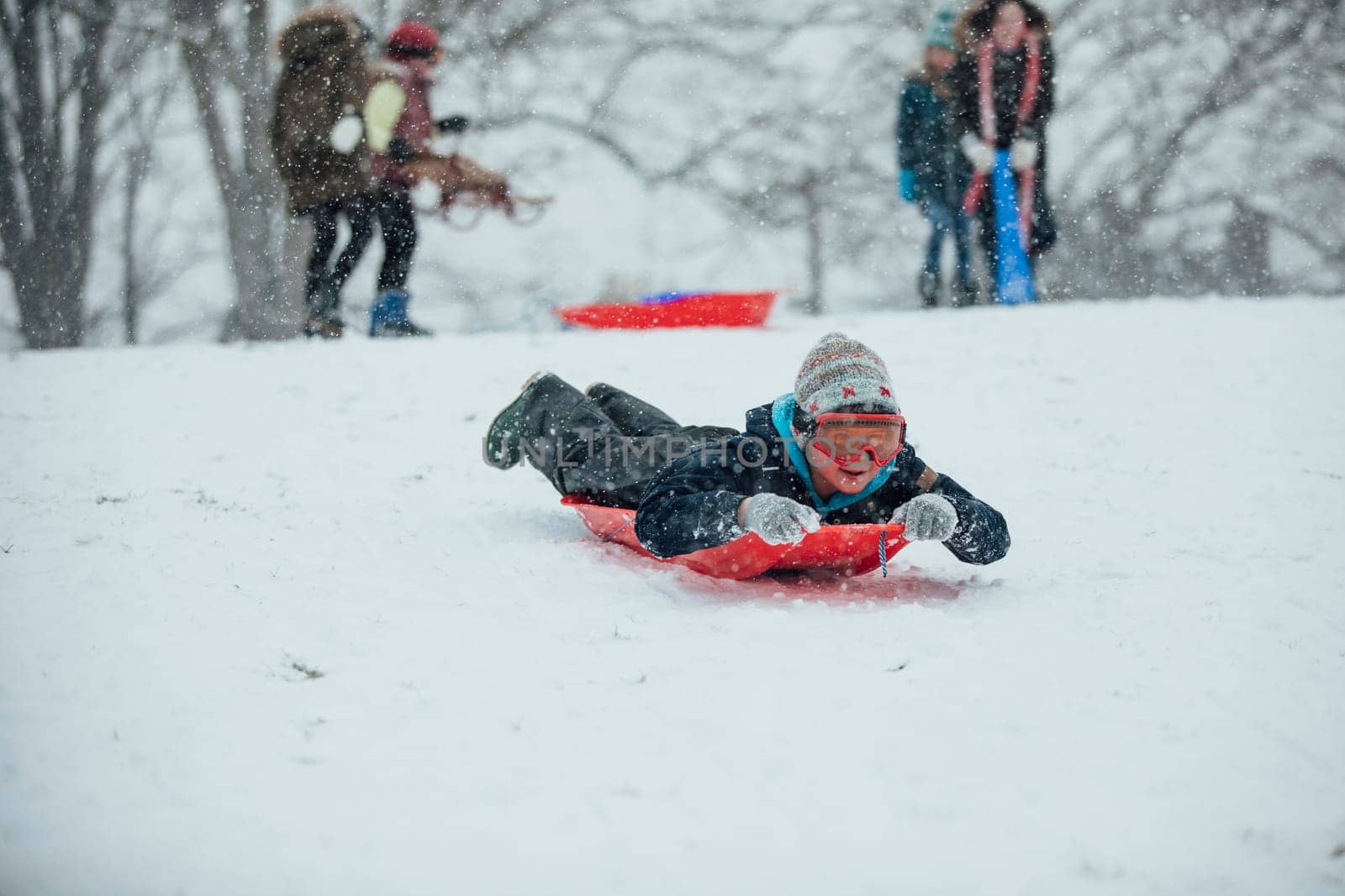 Little boy is lying on a sled, going down a hill in the snow.