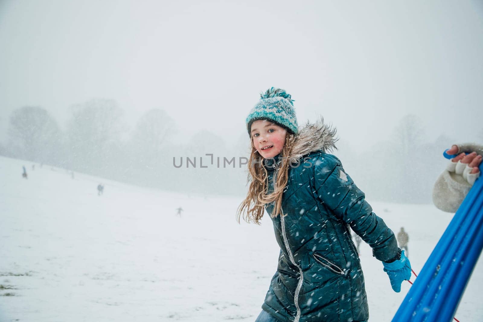 Little girl is looking at the camera while heading uphill with her friends to have a sled race.