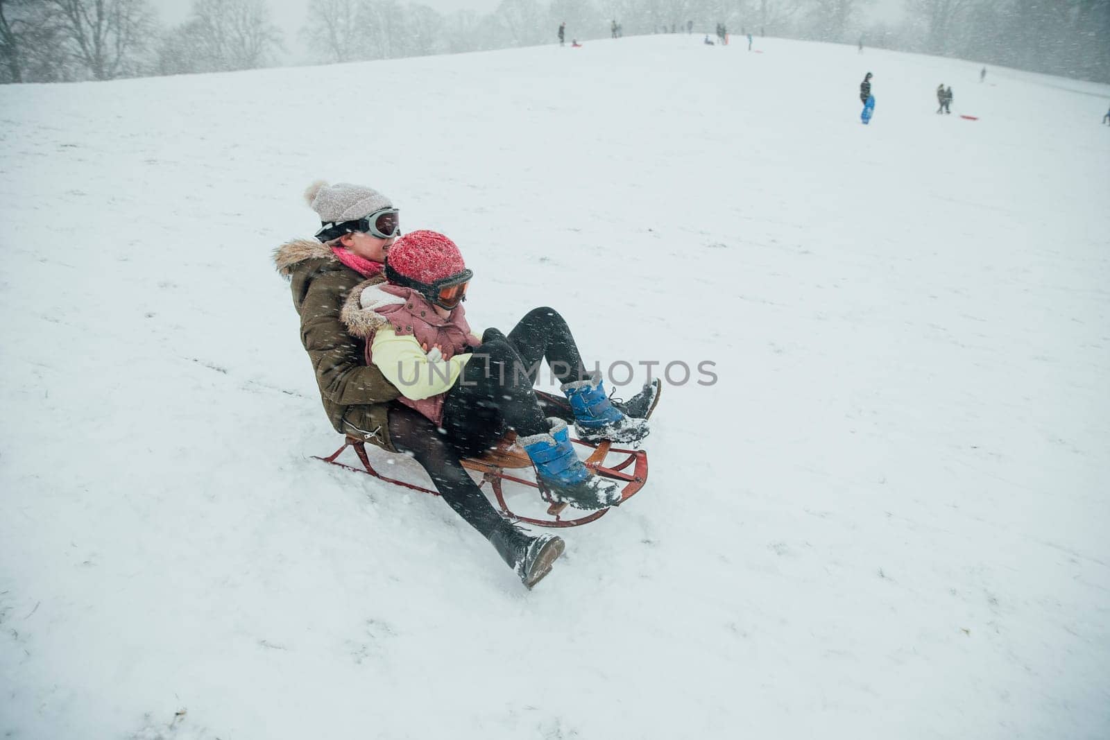 Two girls are holding on to each other as they go down a hill together on a sleigh.