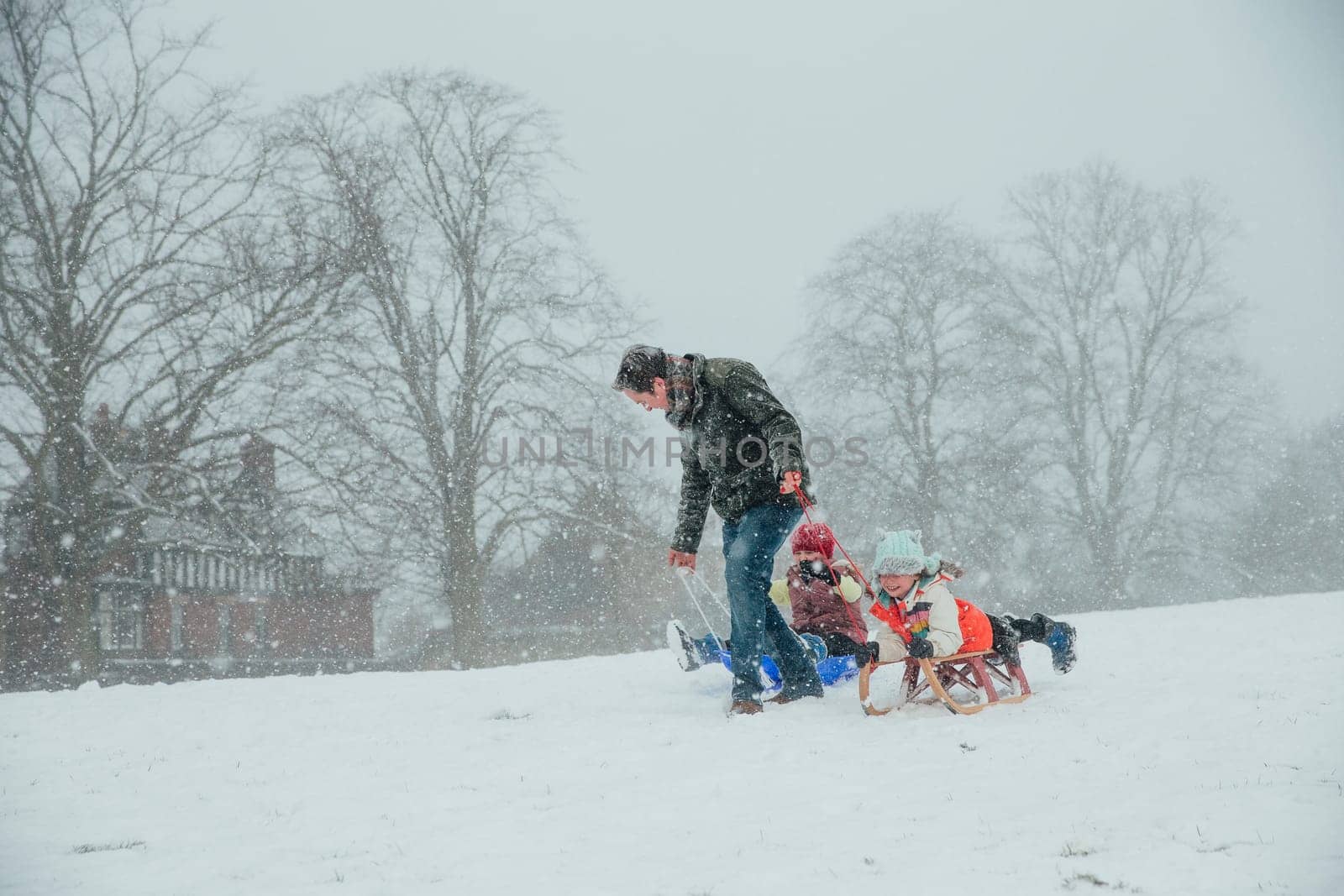 Man is pulling his children along in the snow on sleds.