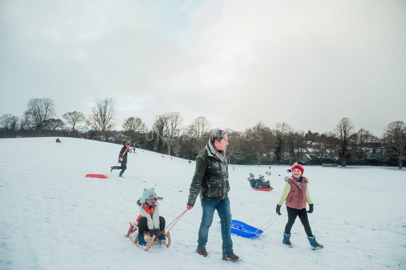 Man is out sledding in the snow with his daughters.