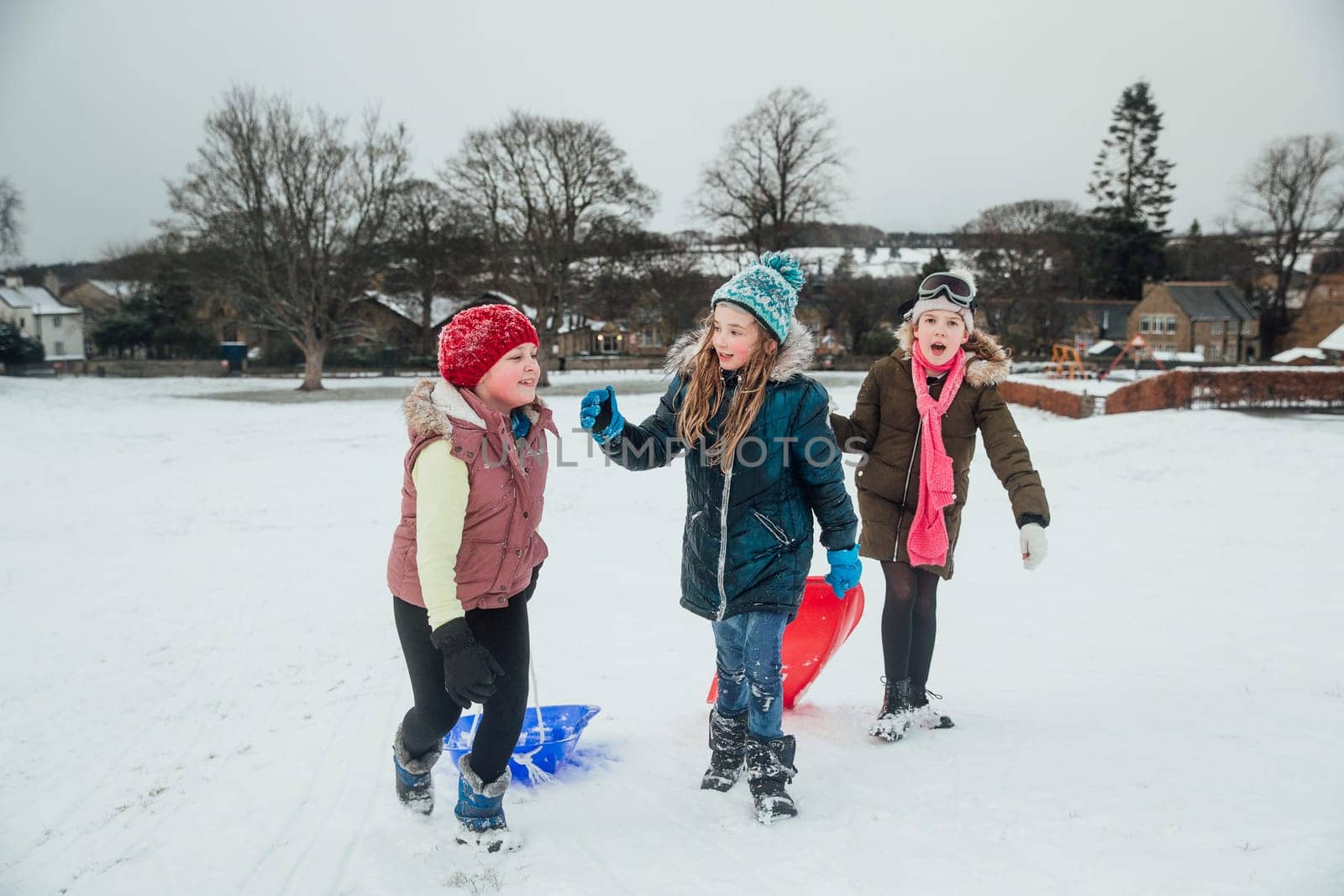Three little girls are talking while they are out playing in the snow with sleds.