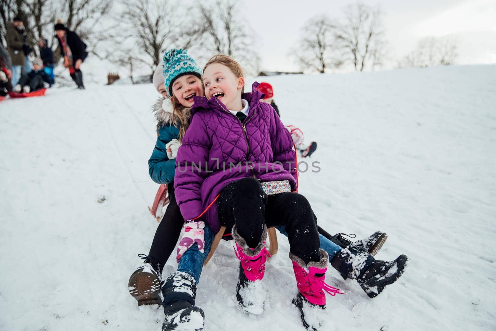 Three little girls are sitting on a sled together, going down a hill in the snow.