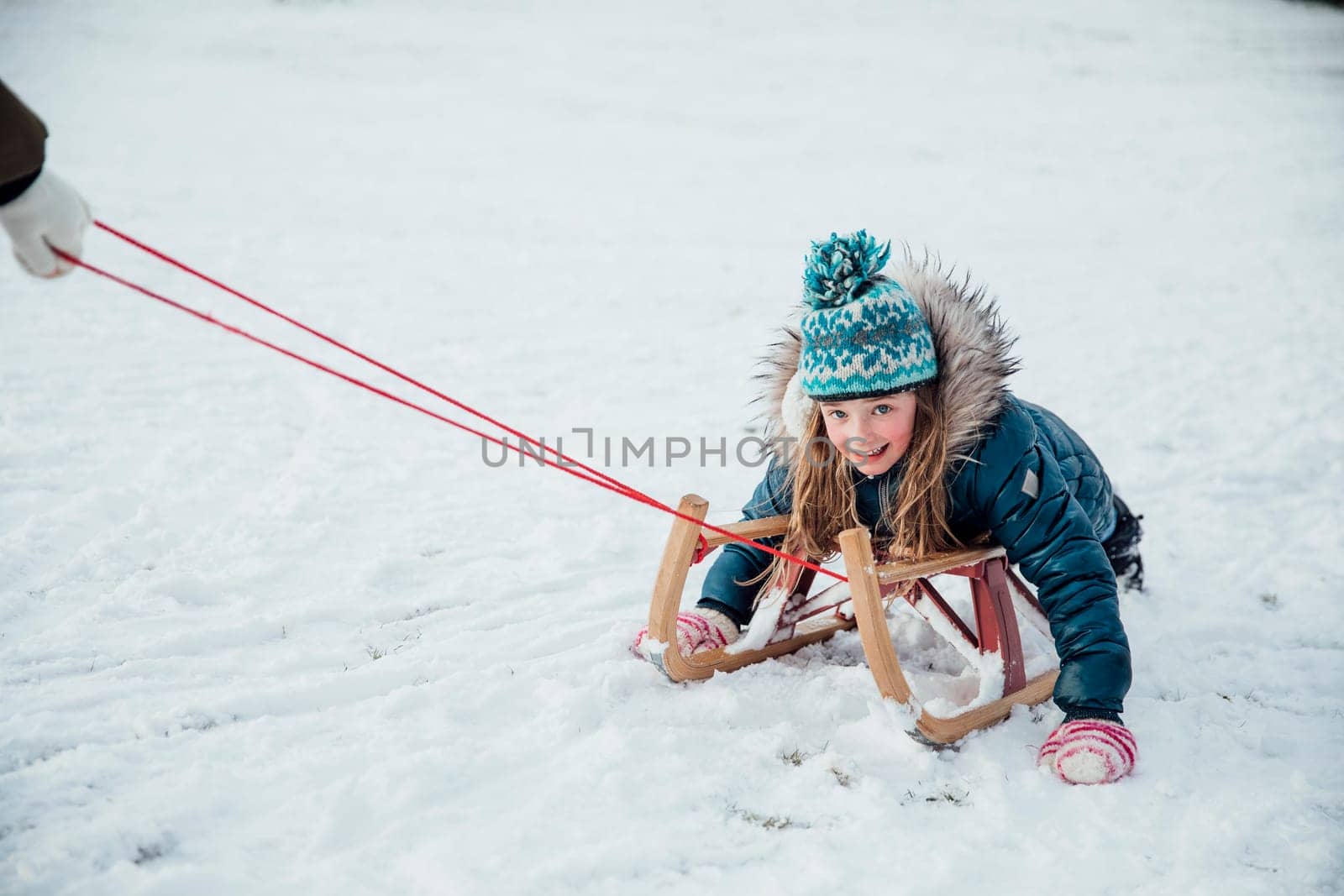Little girl is smiling for the camera while being pulled on a sleigh in the snow.