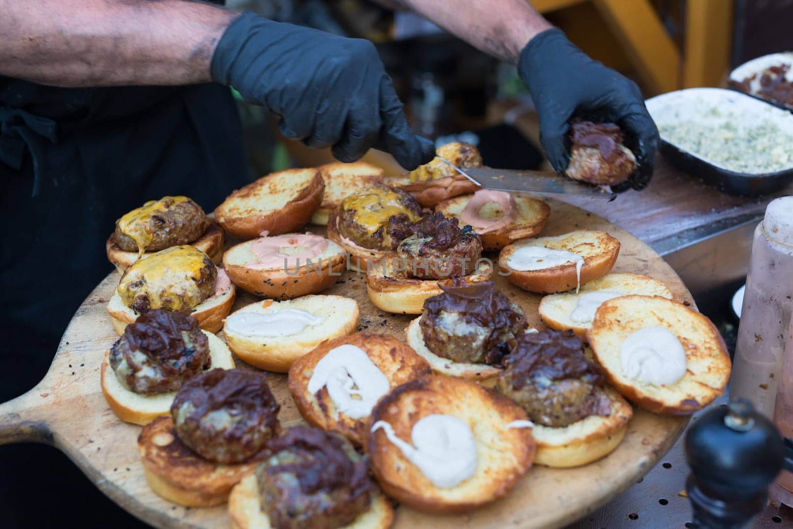 Chef making beef burgers outdoor on open kitchen international food festival event. Street food ready to serve on a food stall.