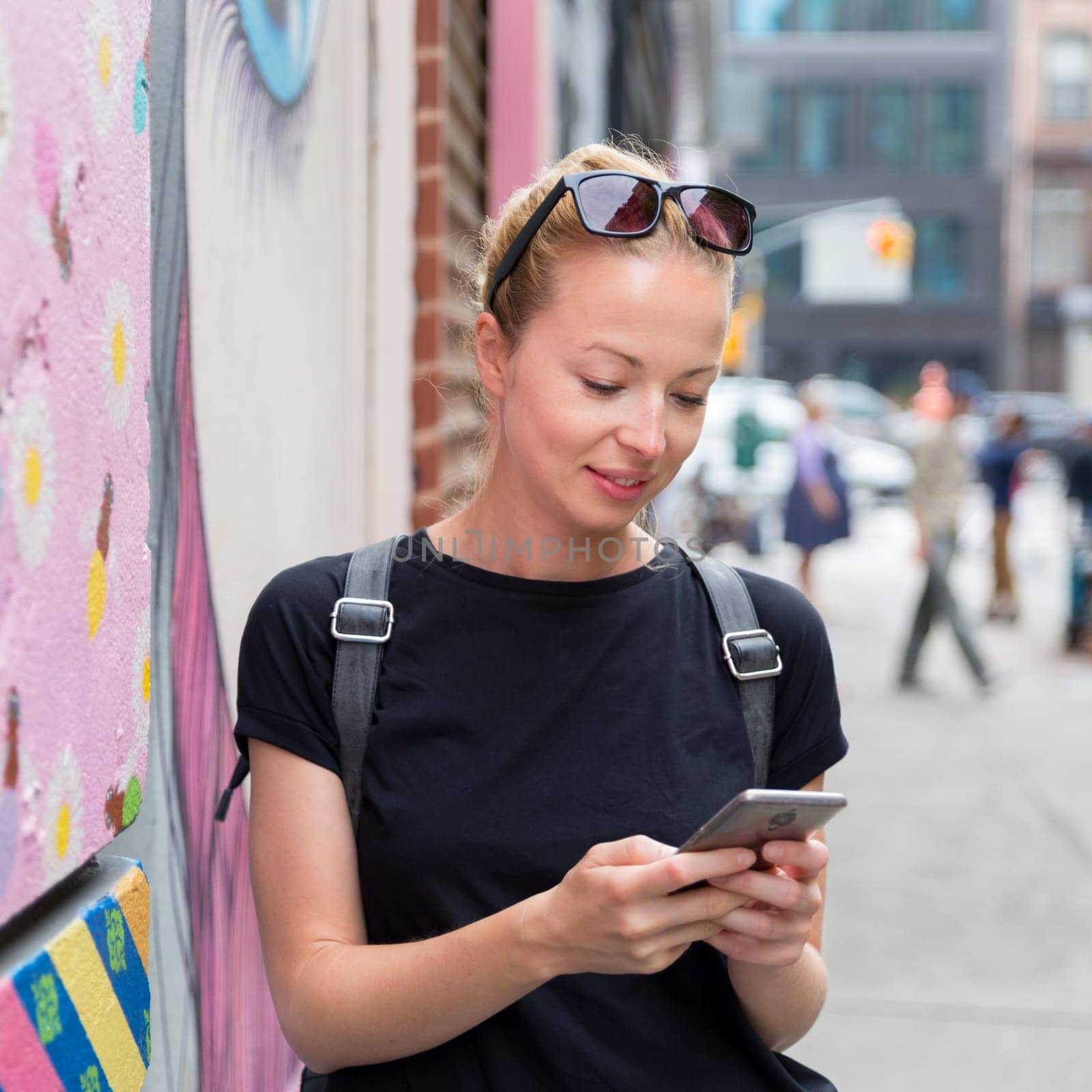 Closeup of female hipster with smart phone. Woman using smartphones against colorful graffiti wall in East Village, New York city, USA.