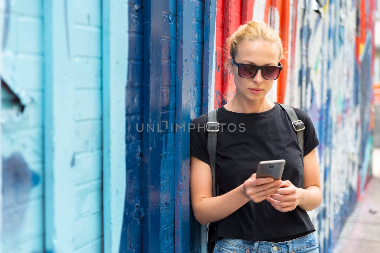 Closeup of female hipster with smart phone. Woman using smartphones against colorful graffiti wall in East Village, New York city, USA.