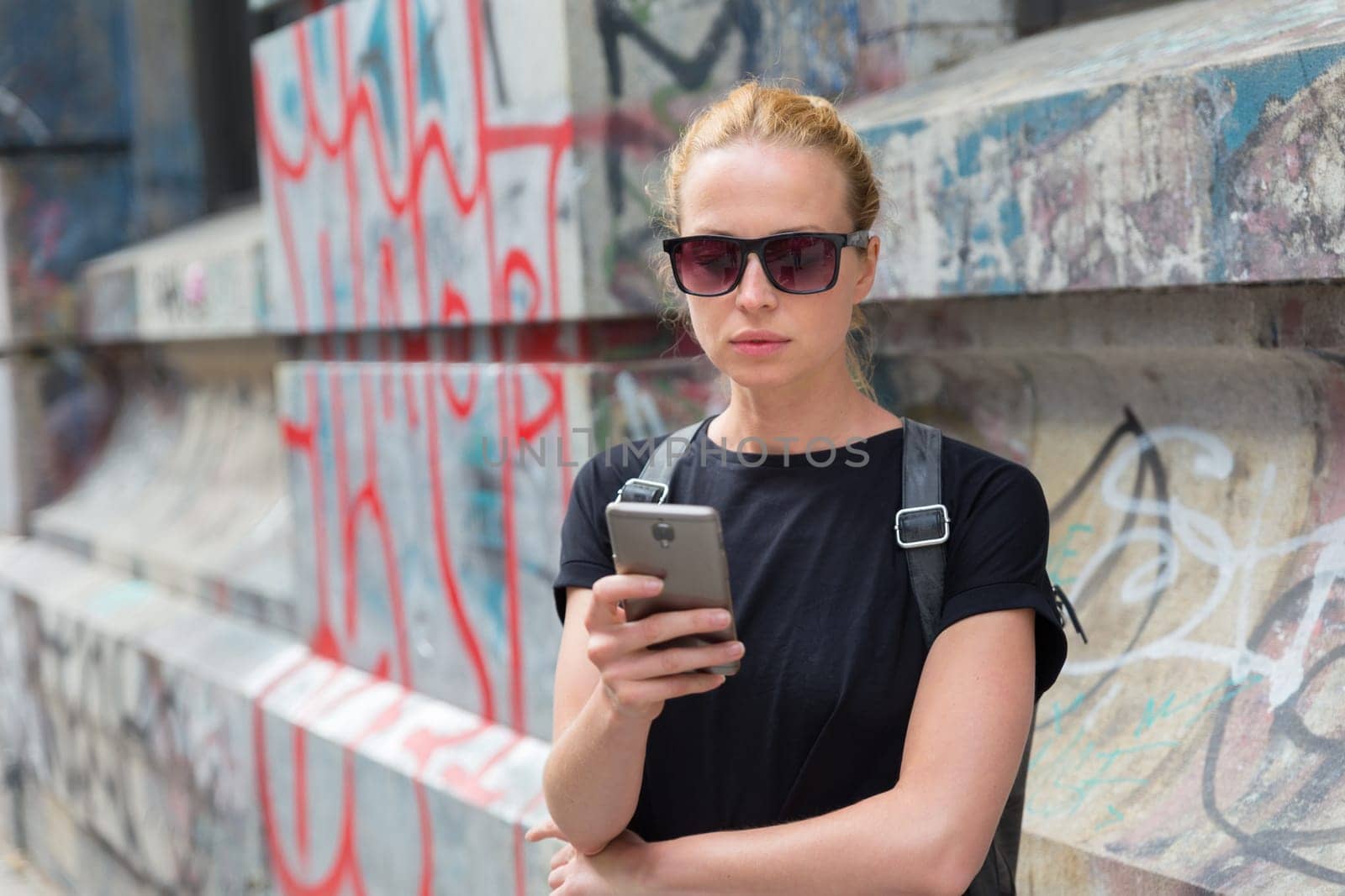 Closeup of female hipster with smart phone. Woman using smartphones against colorful graffiti wall in East Village, New York city, USA.