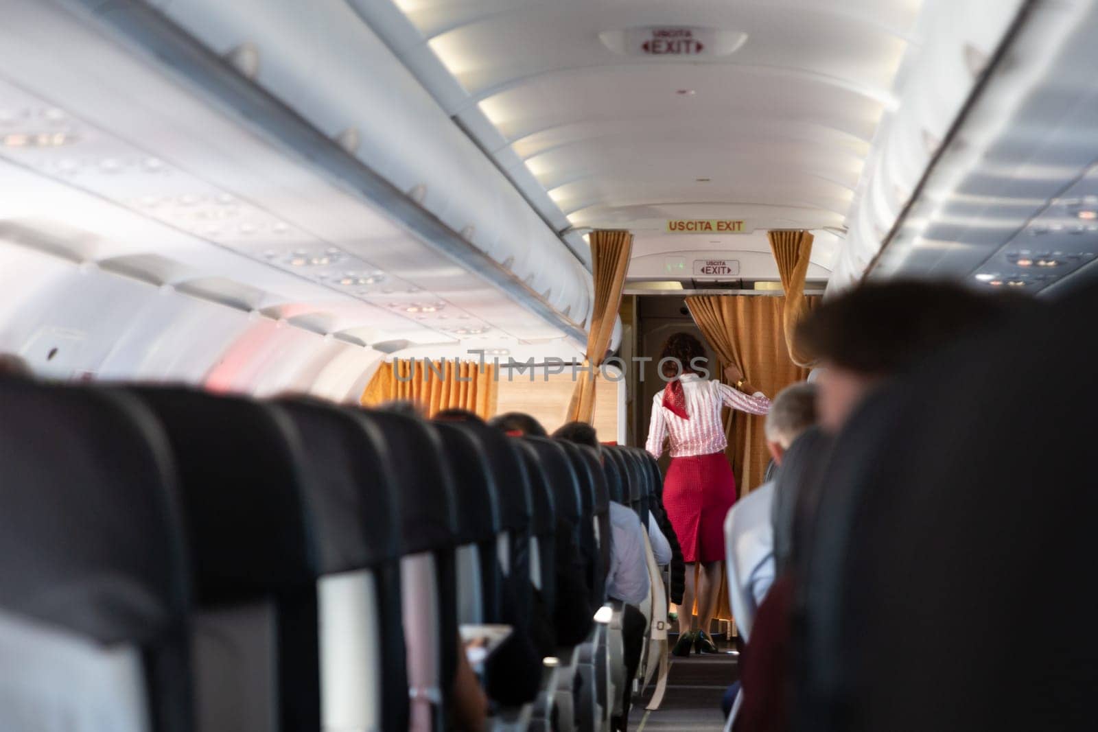 Interior of commercial airplane with passengers on seats during flight. Unrecognizable stewardess in red uniform walking the aisle. Horizontal composition.