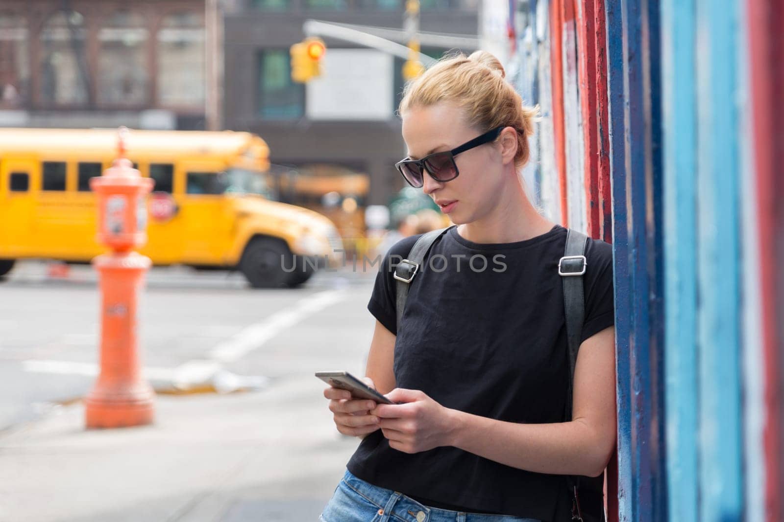 Closeup of female hipster with smart phone. Woman using smartphone against colorful graffiti wall in East Village, New York city, USA.