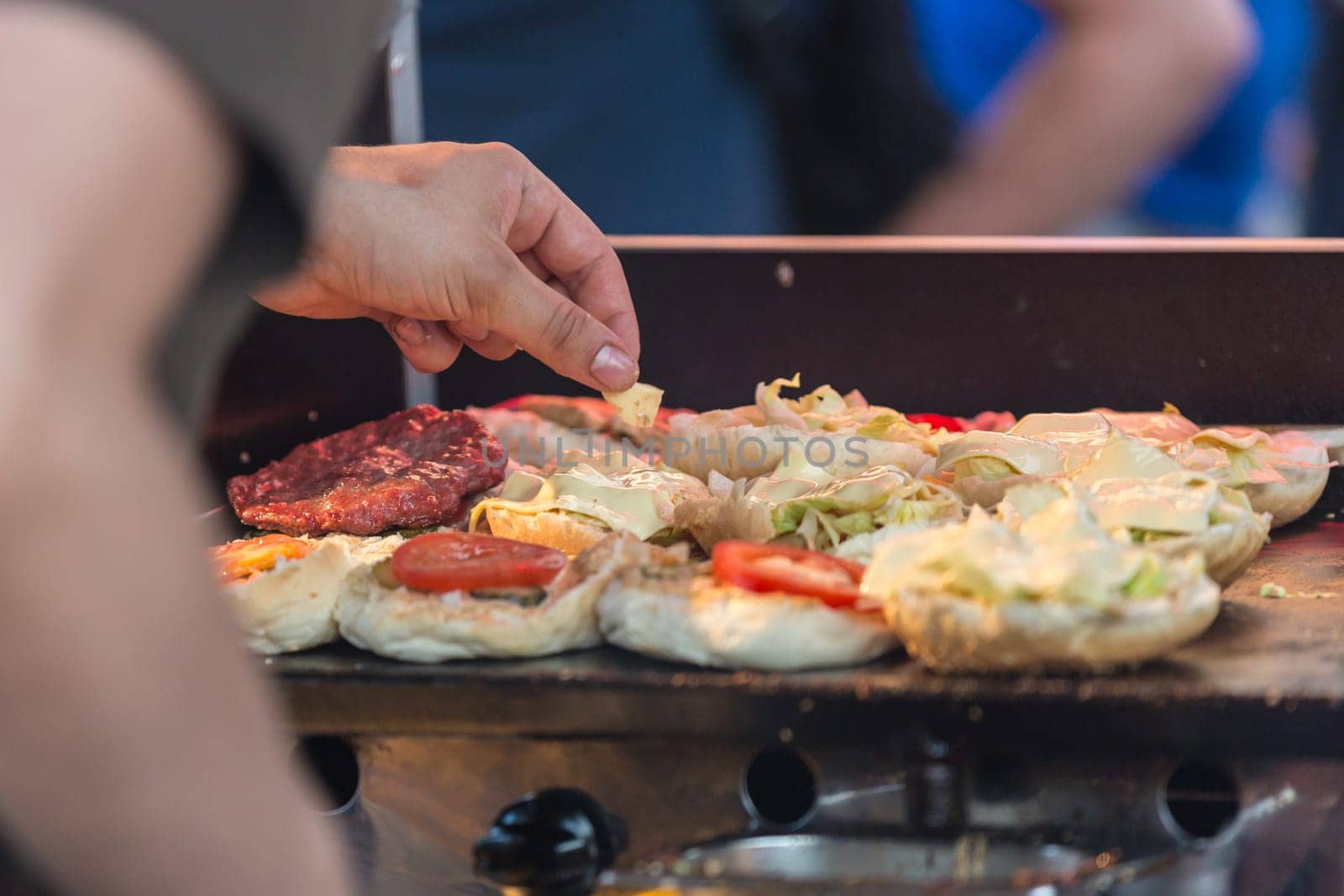 Chef making beef burgers outdoor on open kitchen international food festival event. Street food ready to serve on a food stall.