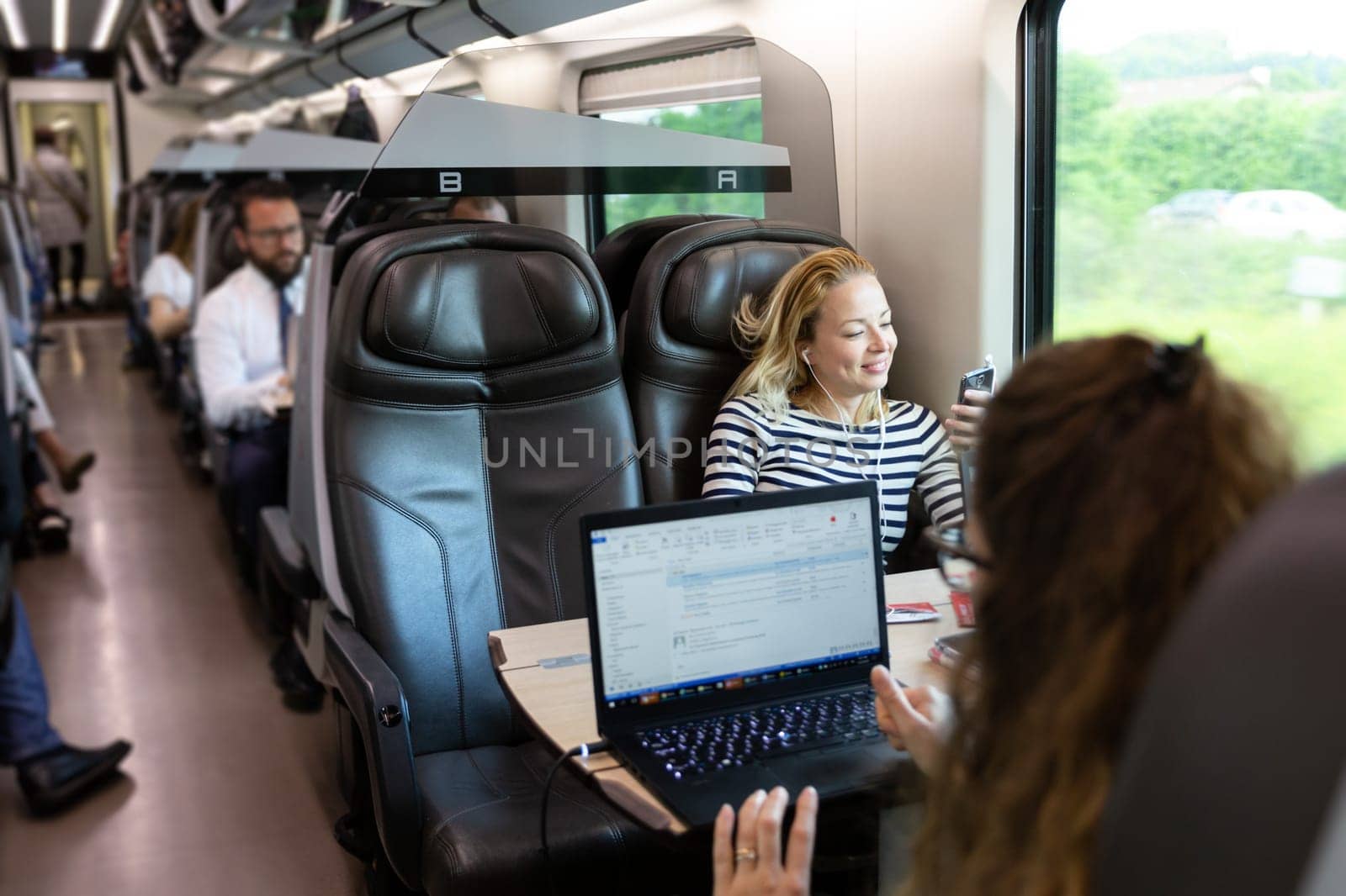 Businesswoman communicating on cellphone using headphone set while traveling by train in business class seat.