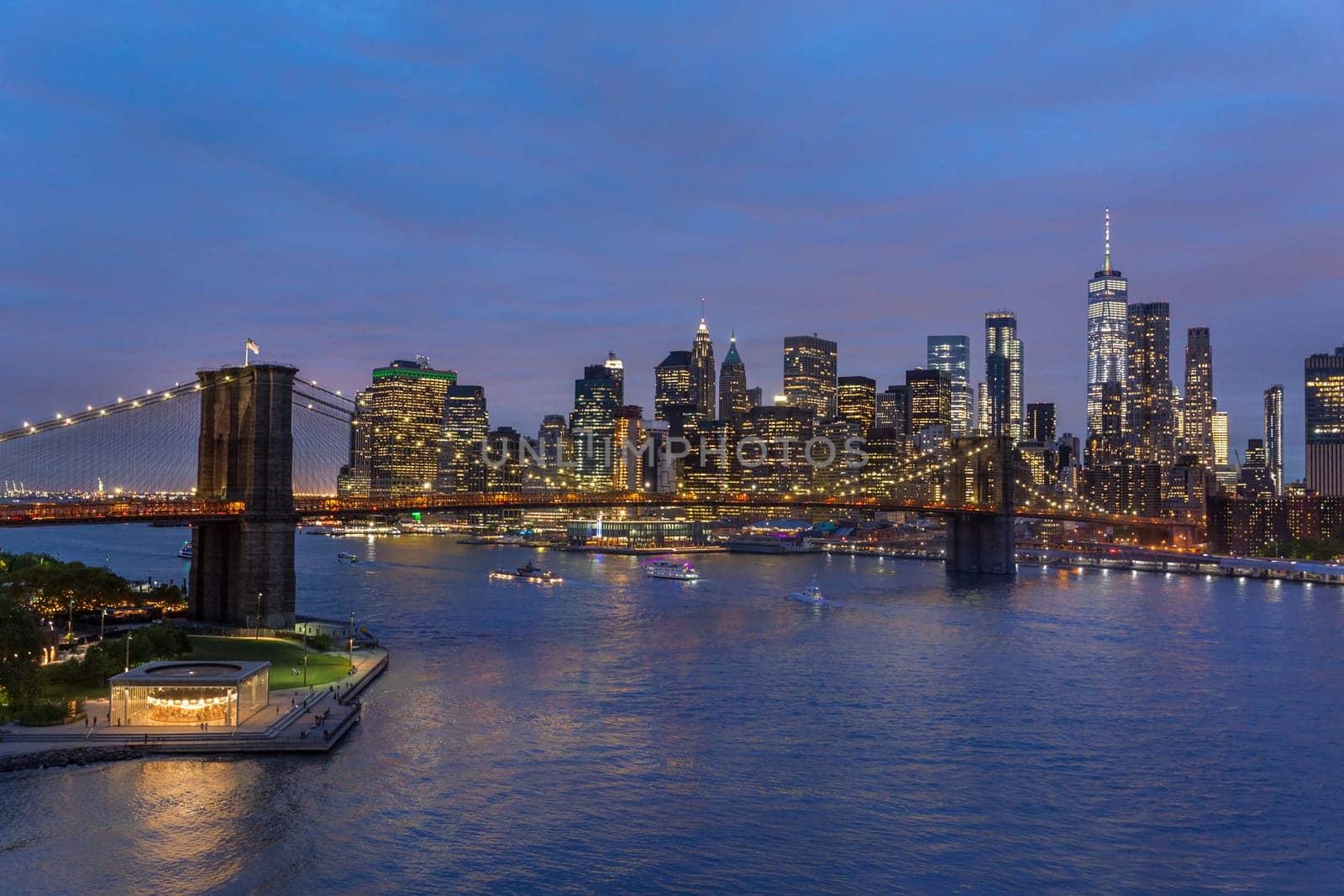 Brooklyn park, Brooklyn Bridge, Janes Carousel and Lower Manhattan skyline at night seen from Manhattan bridge, New York city, USA. Wide angle panoramic image.