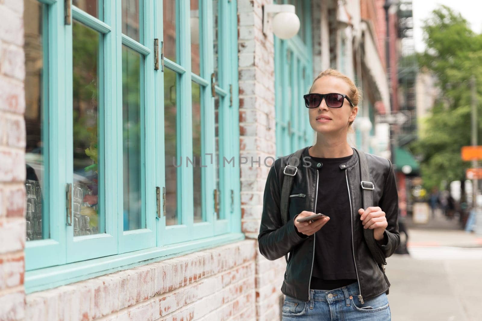 Beautiful blond young female tourist using smart phone app guite on city break weekend trip to New York.