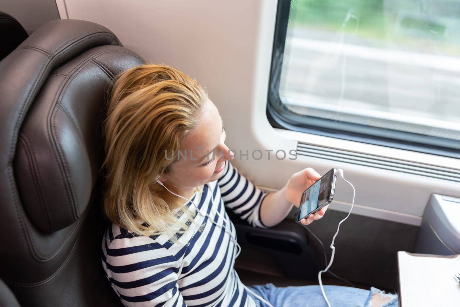 Woman communicating on cellphone using headphone set while traveling by train in business class seat.