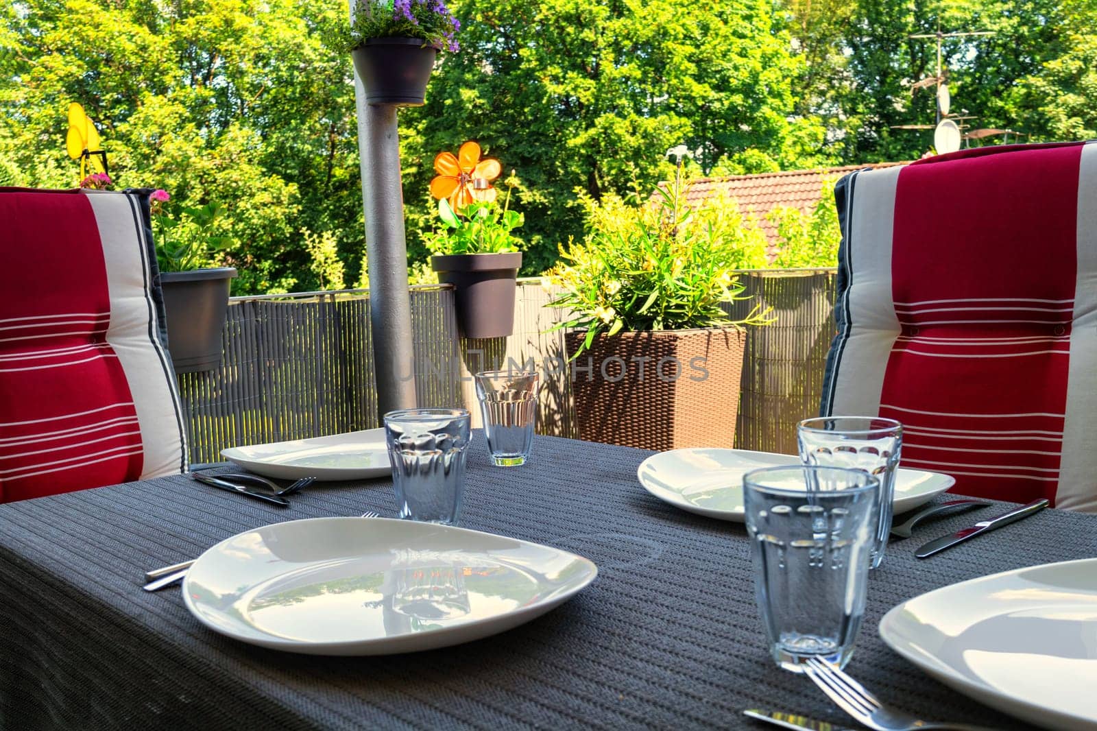 Covered balcony table with white plates, drinking glasses and dining table with two chairs with modern seat covers.