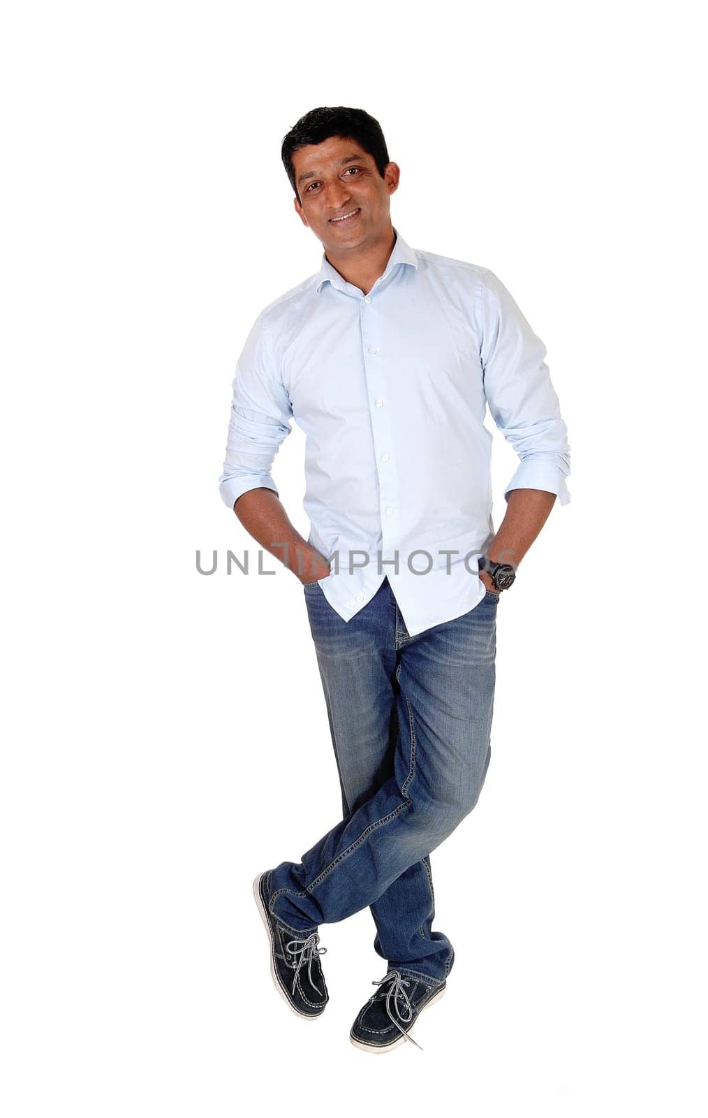 A tall East Indian man standing relaxed in jeans and blue shirt with.his hands in his pocket, isolated for white background.