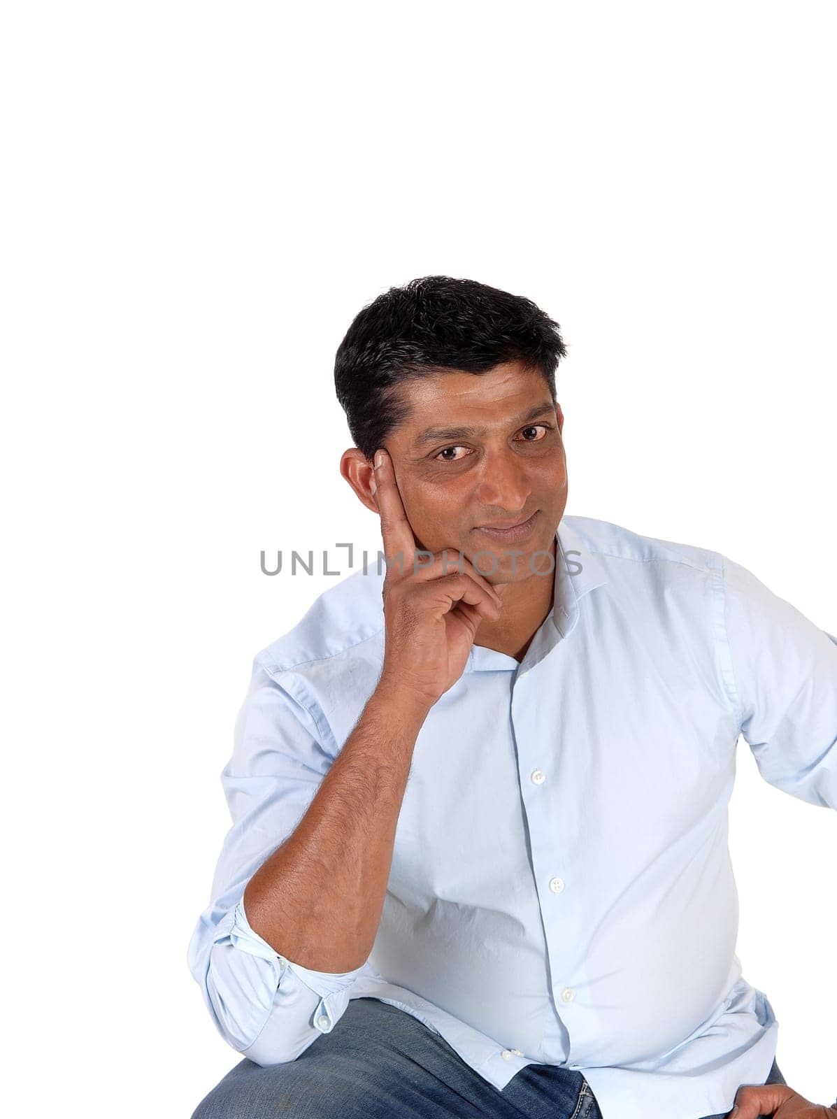 A closeup image of a good looking man in a blue shirt and jeans with.one hand on his face, isolated for white background.