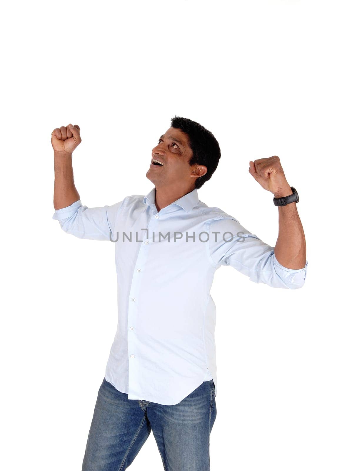 A very exited man in jeans and a blue shirt standing with his fists in a.joyful and cheerful way about his great lack, isolated over white.