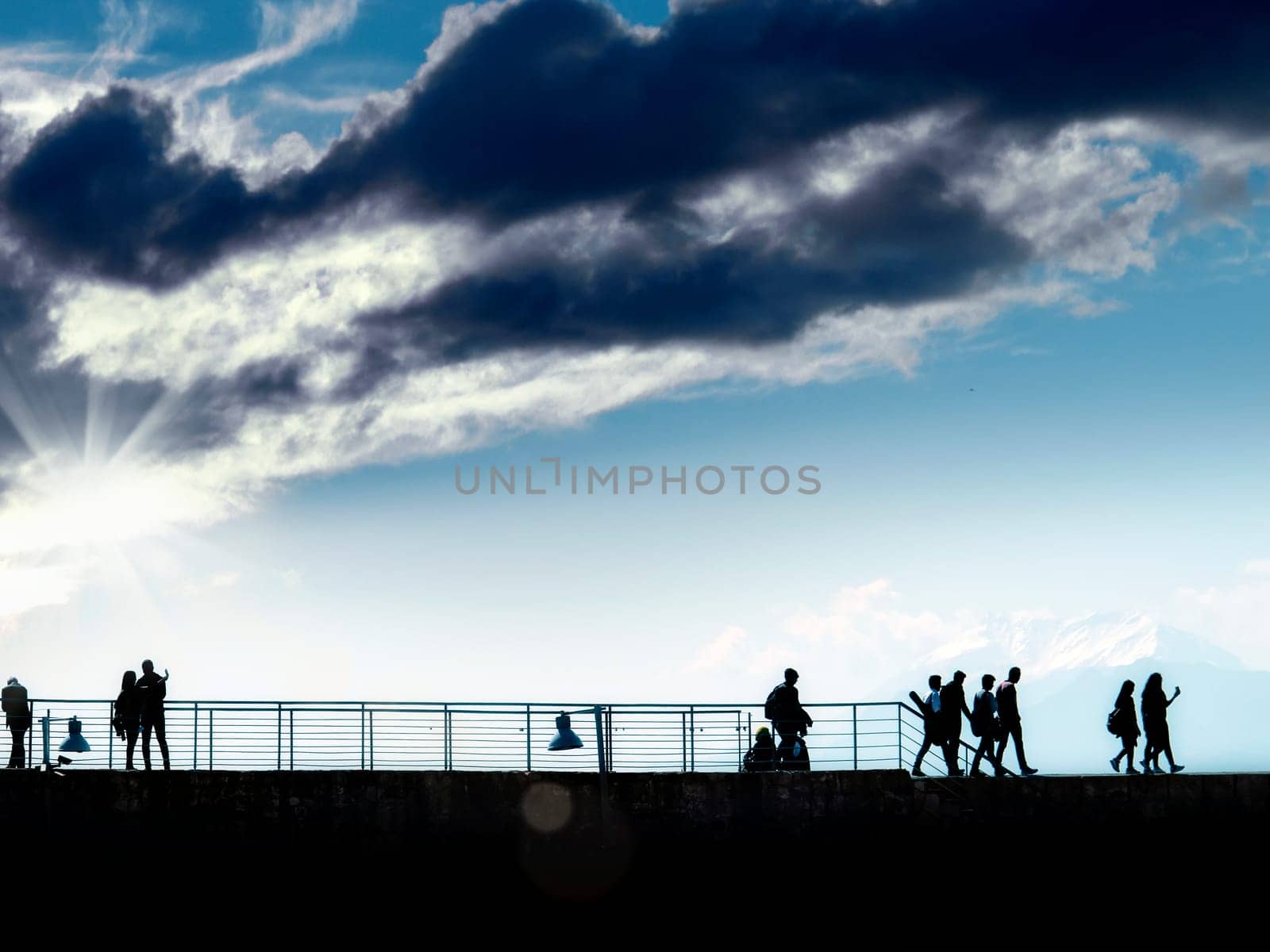 silhouetted people walking over sunny and cloudy blue sky