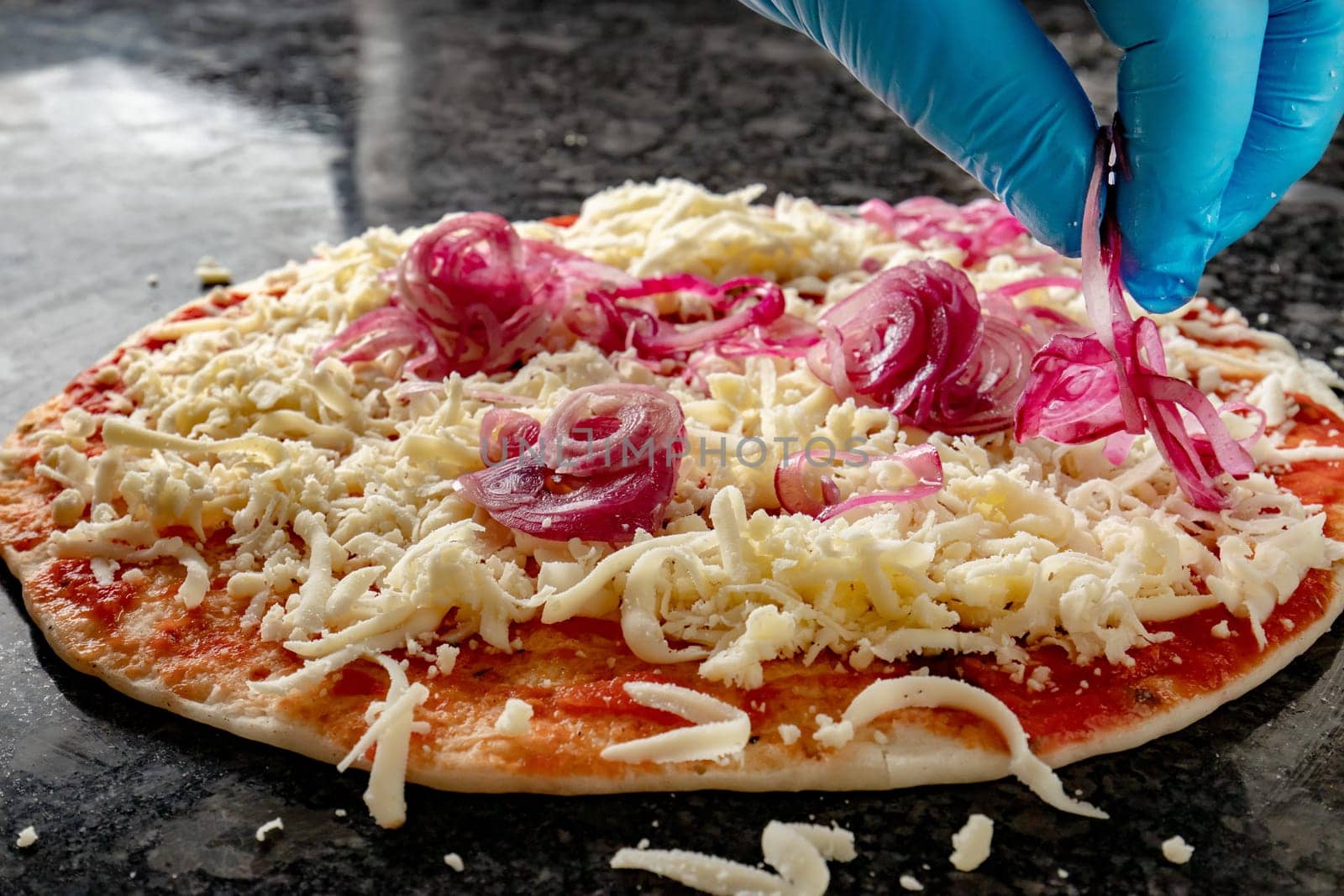 Hand with glove spread onion over the cheese pizza