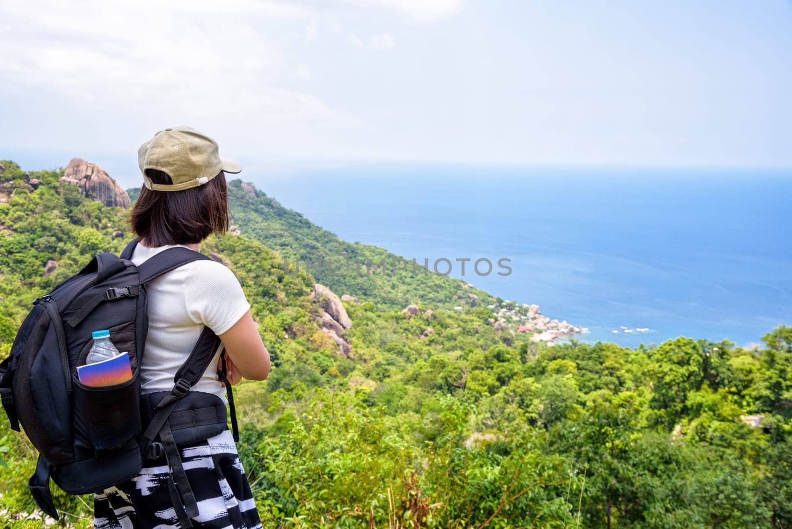 Women tourist with a backpack wear cap standing look at beautiful nature landscape blue sea under the summer sky from high scenic viewpoint at Koh Tao in Surat Thani, Thailand
