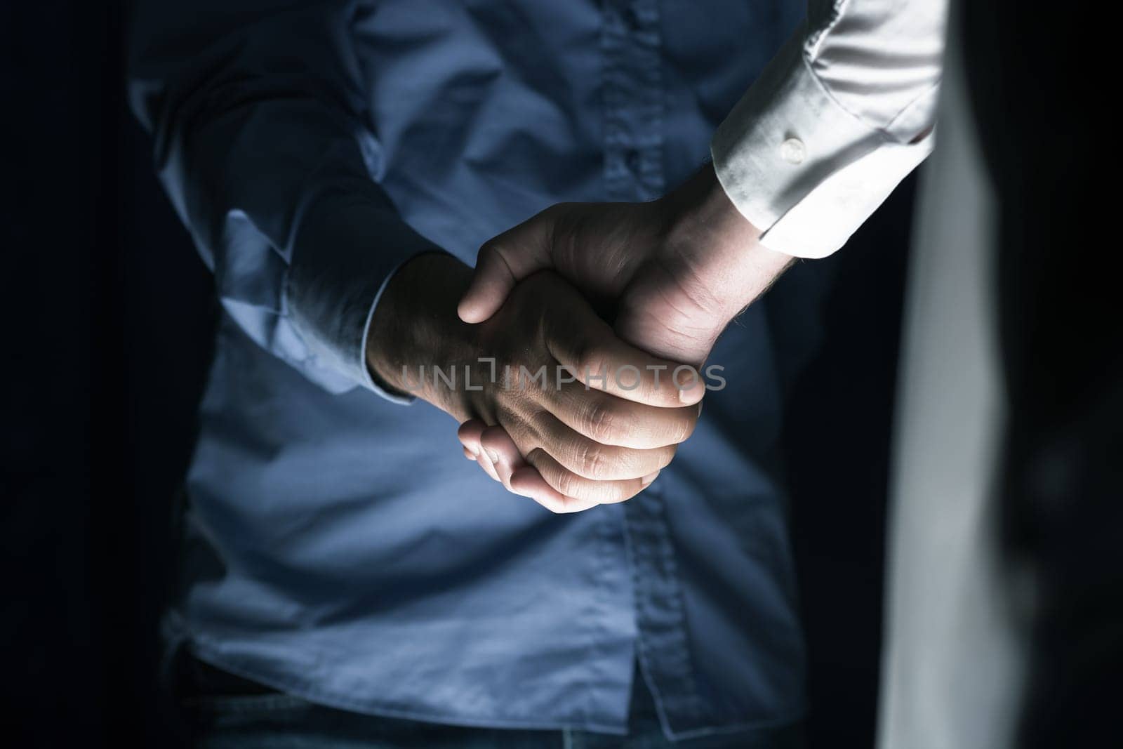 Handshaking of two business people. Partnership - Teamwork. Greeting, Form Of Communication. Light in scene come from down.