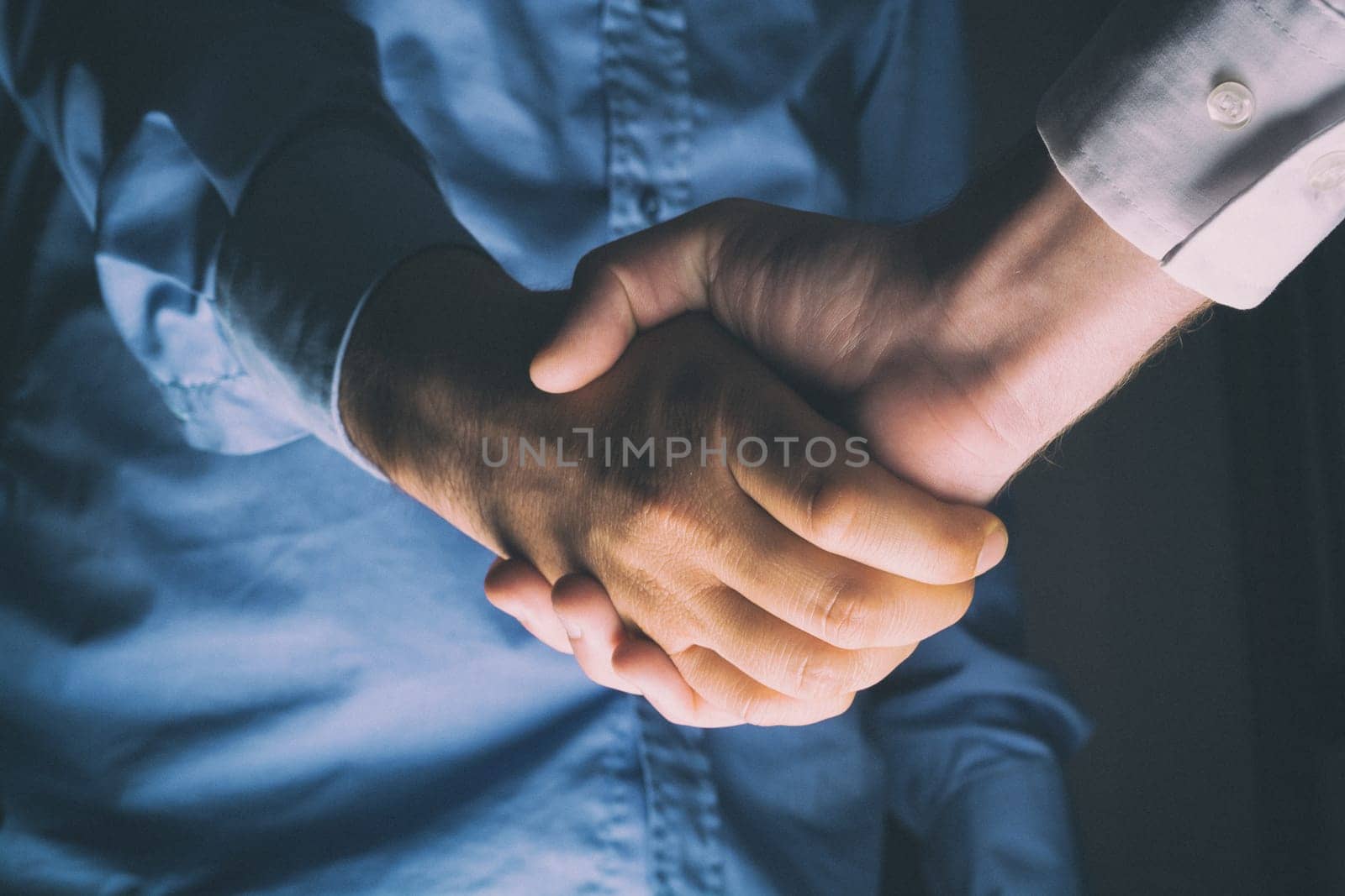 Handshaking of two business people. Partnership - Teamwork. Greeting, Form Of Communication. Light in scene come from down.