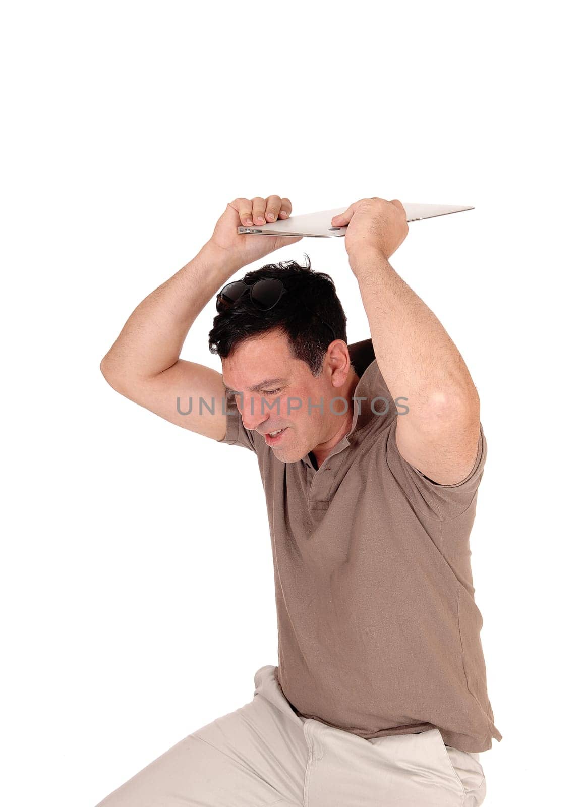 A very frustrated man sitting on a chair and likes to throw away his new.laptop, holding it over his head, isolated for white background.