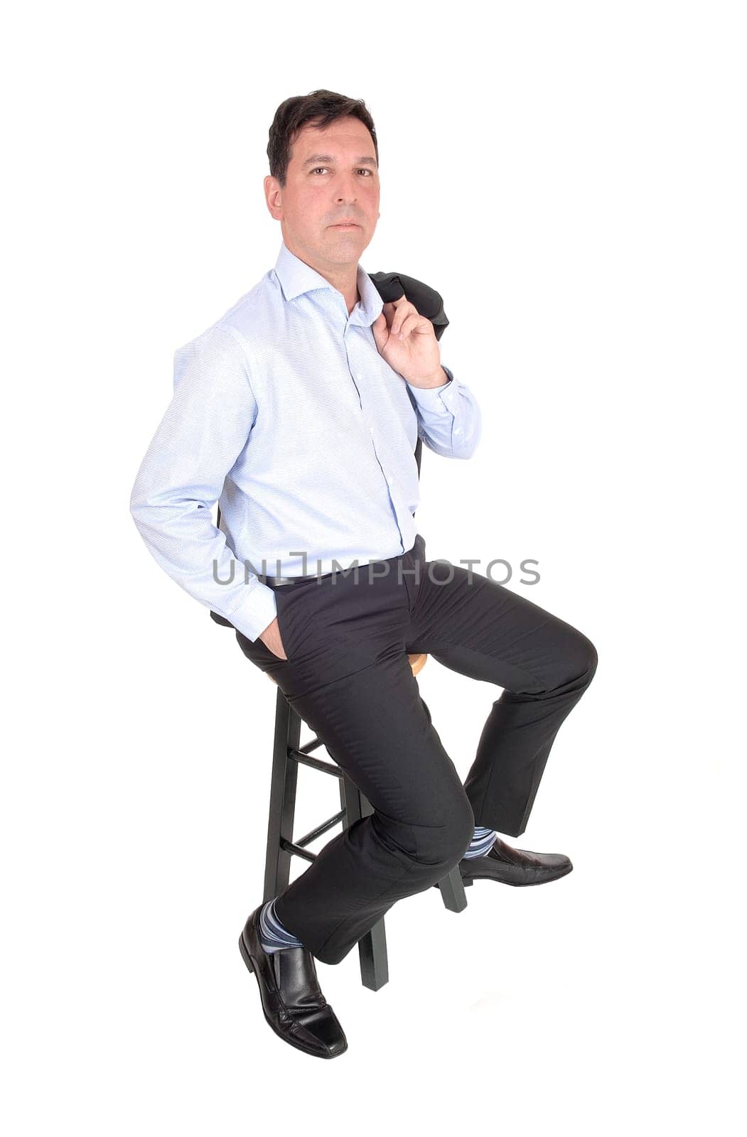 A tall middle age business man sitting on a chair with his jacket over.his shoulder and hand in pocket, isolated for white background.